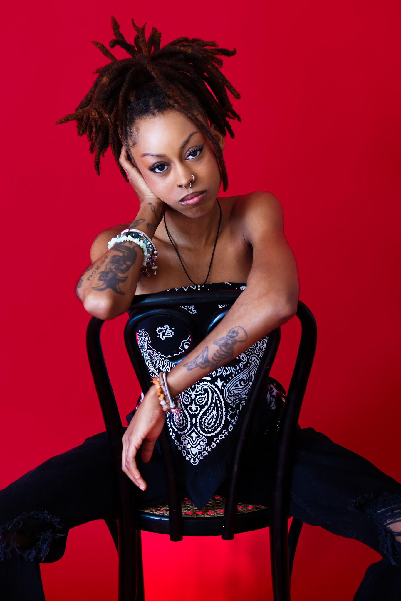Artistic portrait series against red background wearing bandana top and dark denim.