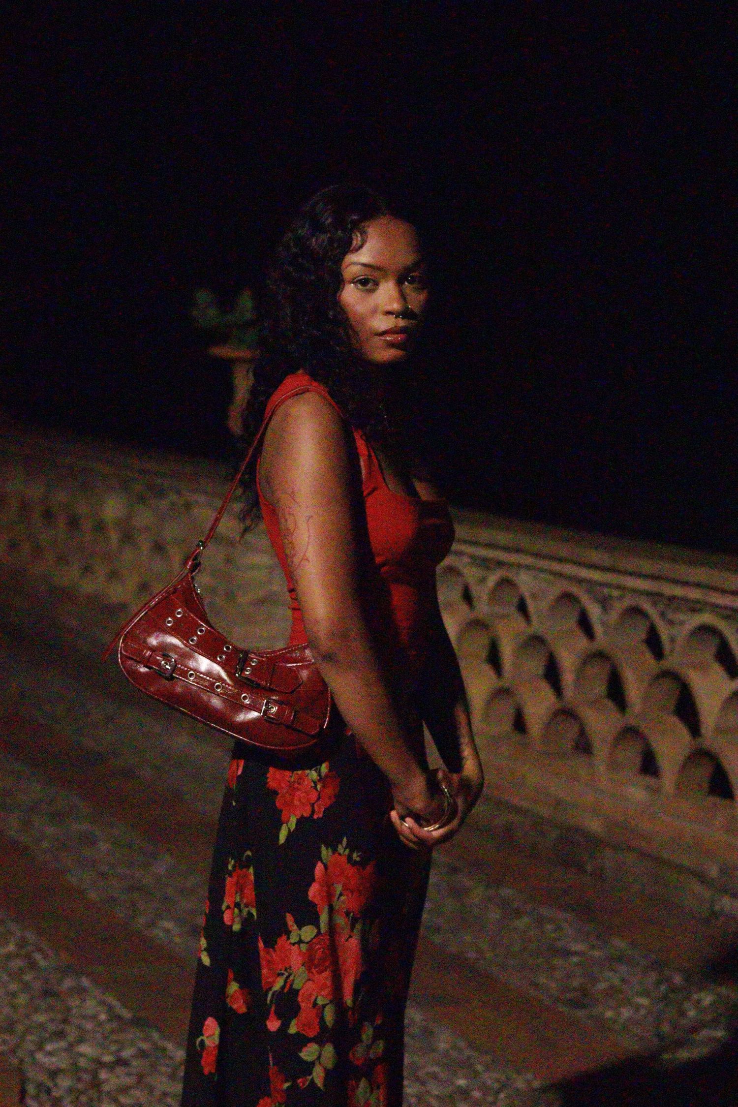 A figure in a floral dress poses dramatically against a dark background at night.