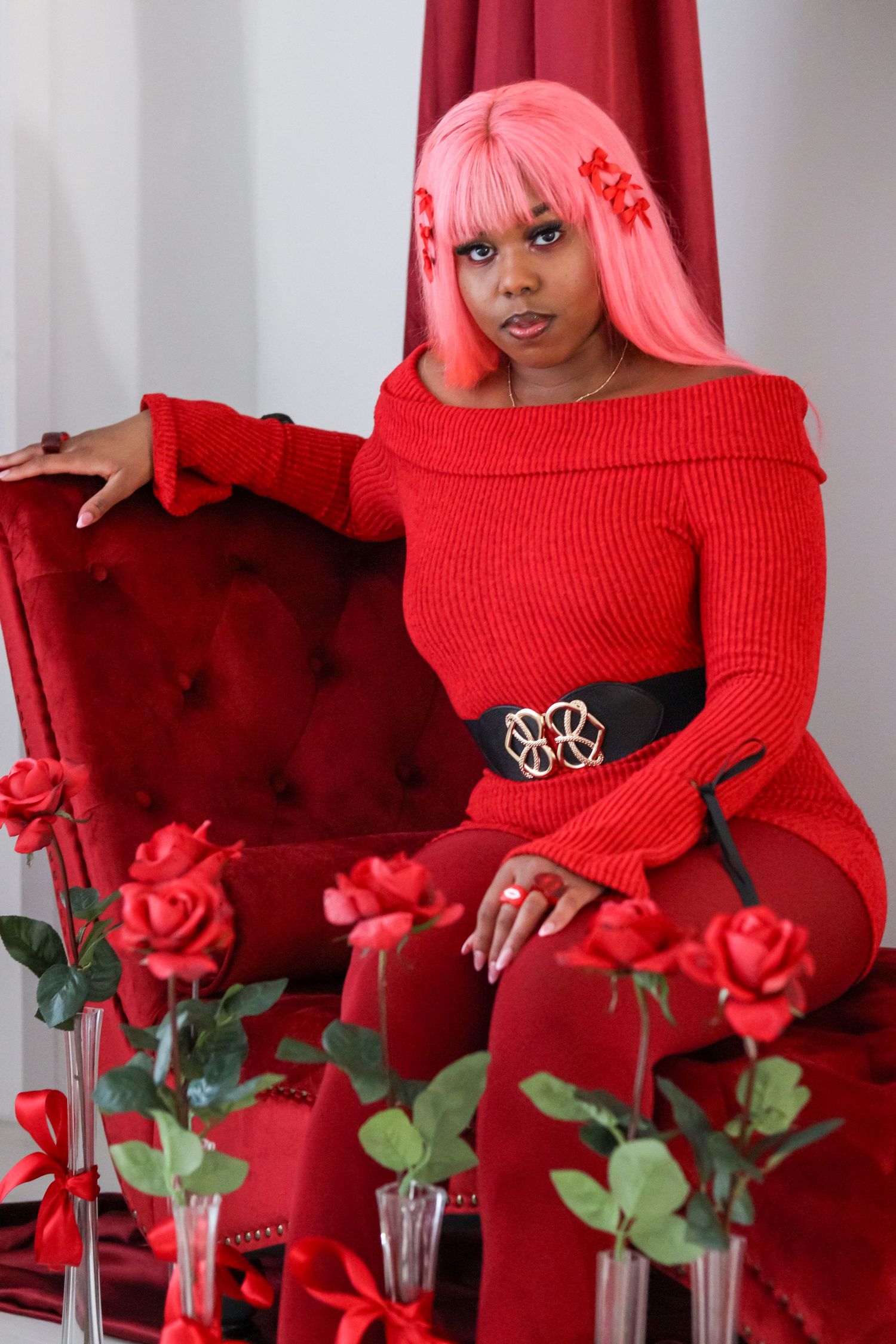 Red aesthetic photoshoot with roses and person wearing bright red sweater against red backdrop.