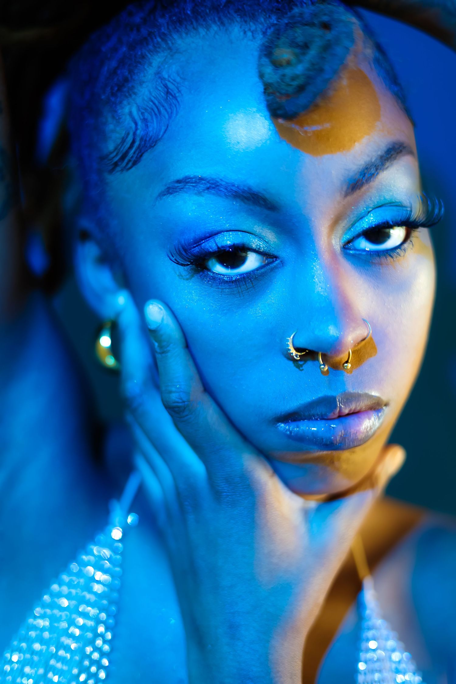 Artistic portrait with blue lighting showcasing sparkly jewelry and dramatic makeup.