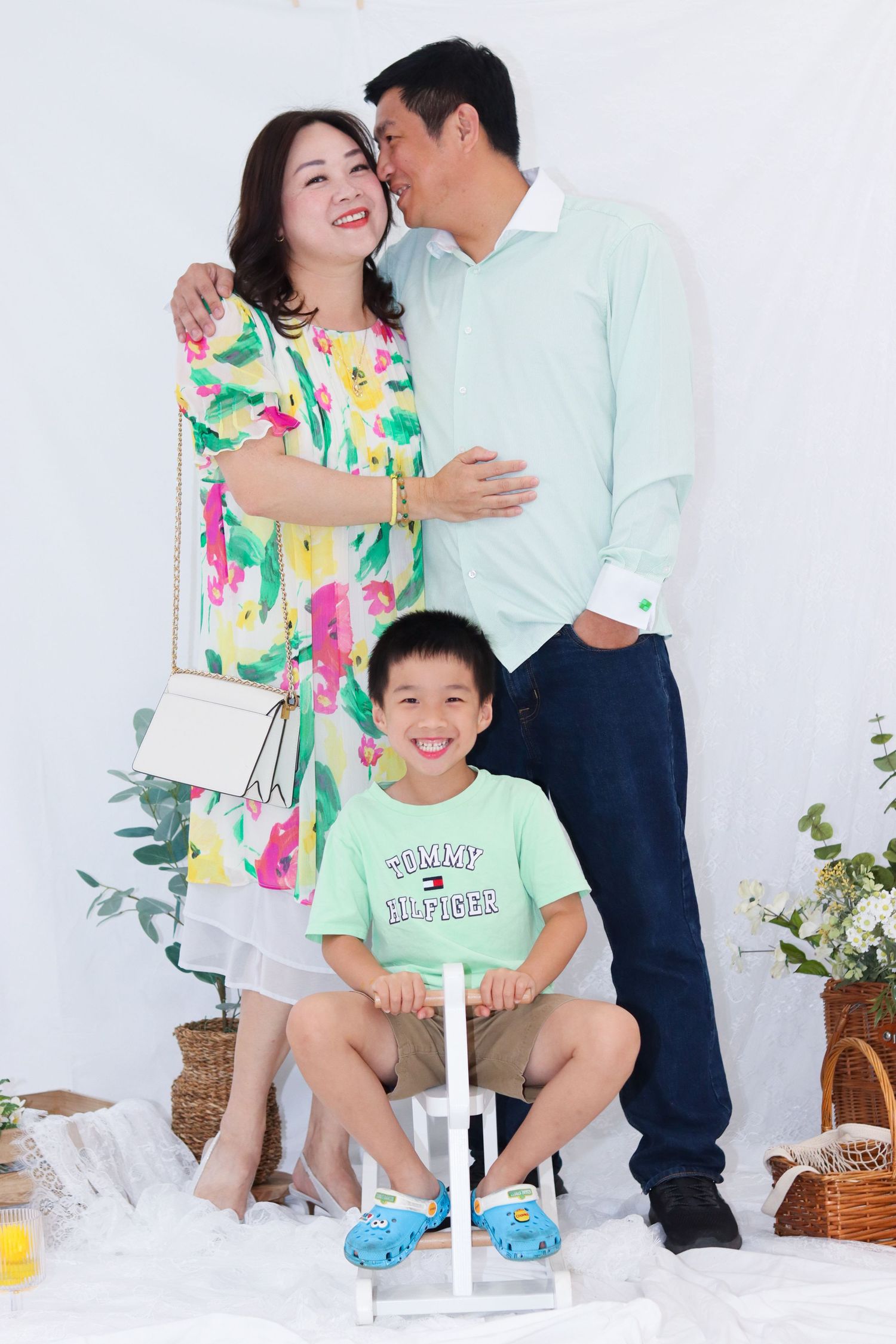 Family wearing coordinating mint green outfits posing together on white set with decorative plants.