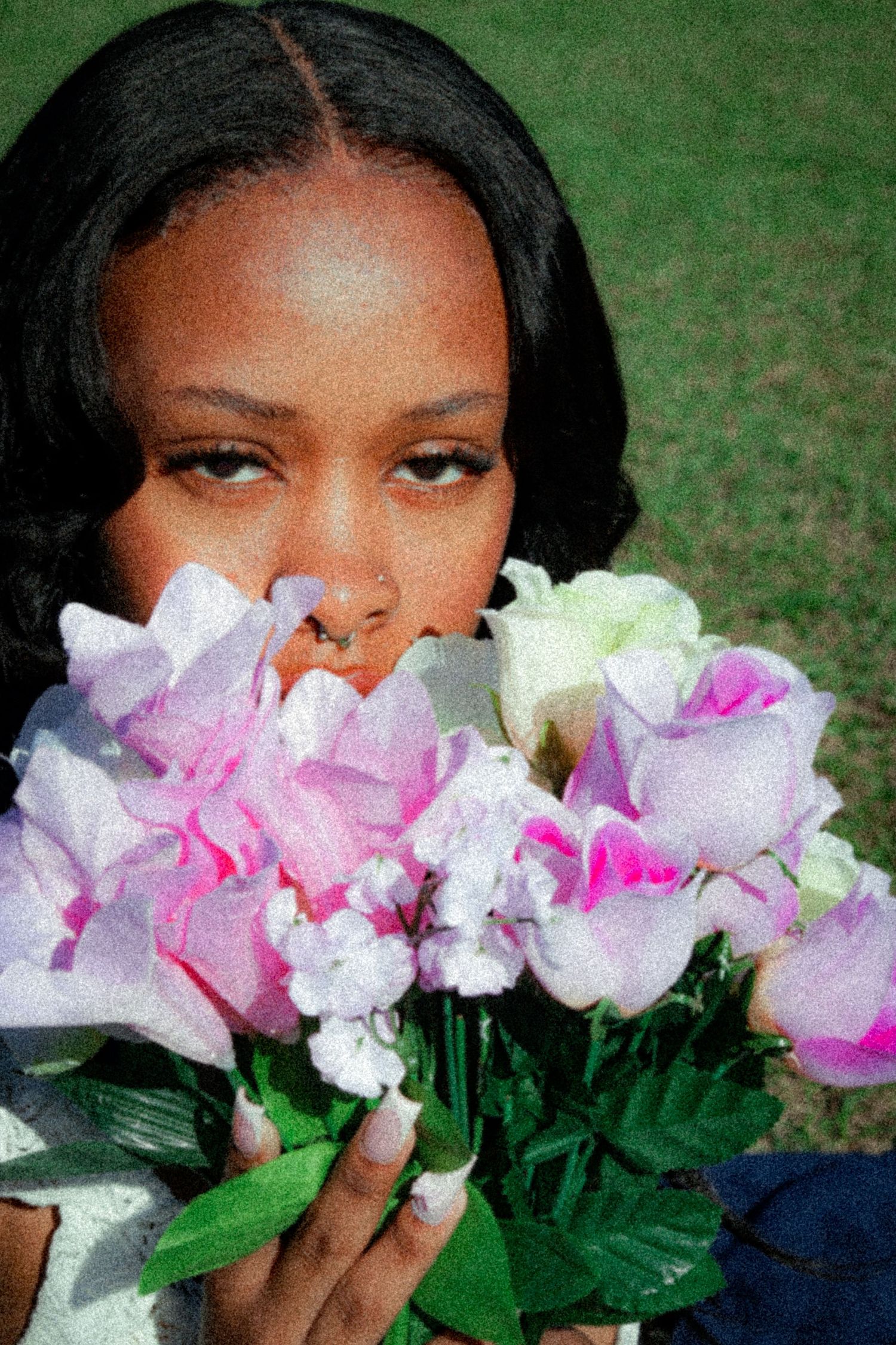 Pink and white flowers held in front of a grassy outdoor setting.