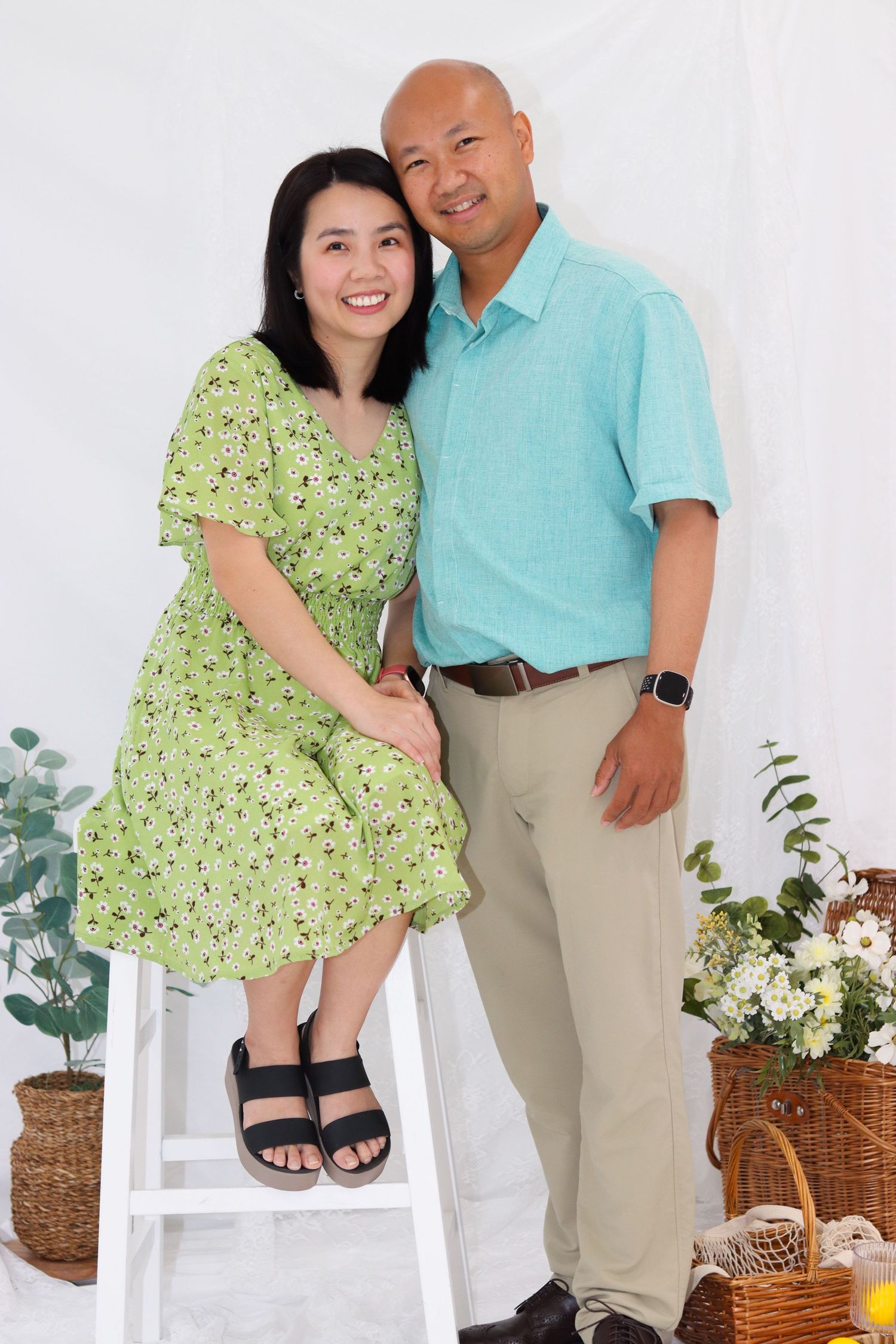 Family portrait in coordinated green and turquoise outfits posing against white background with plants.