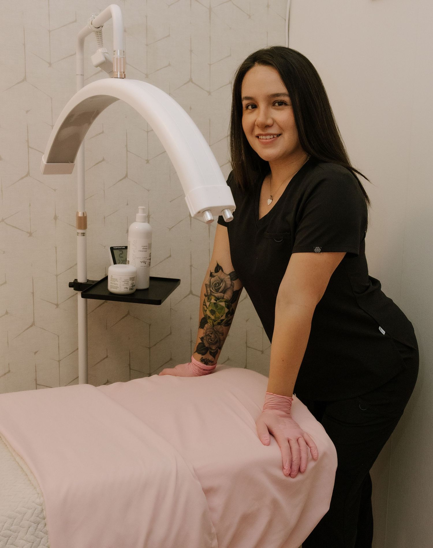 Person in dark clothing preparing pink treatment table in white professional space.