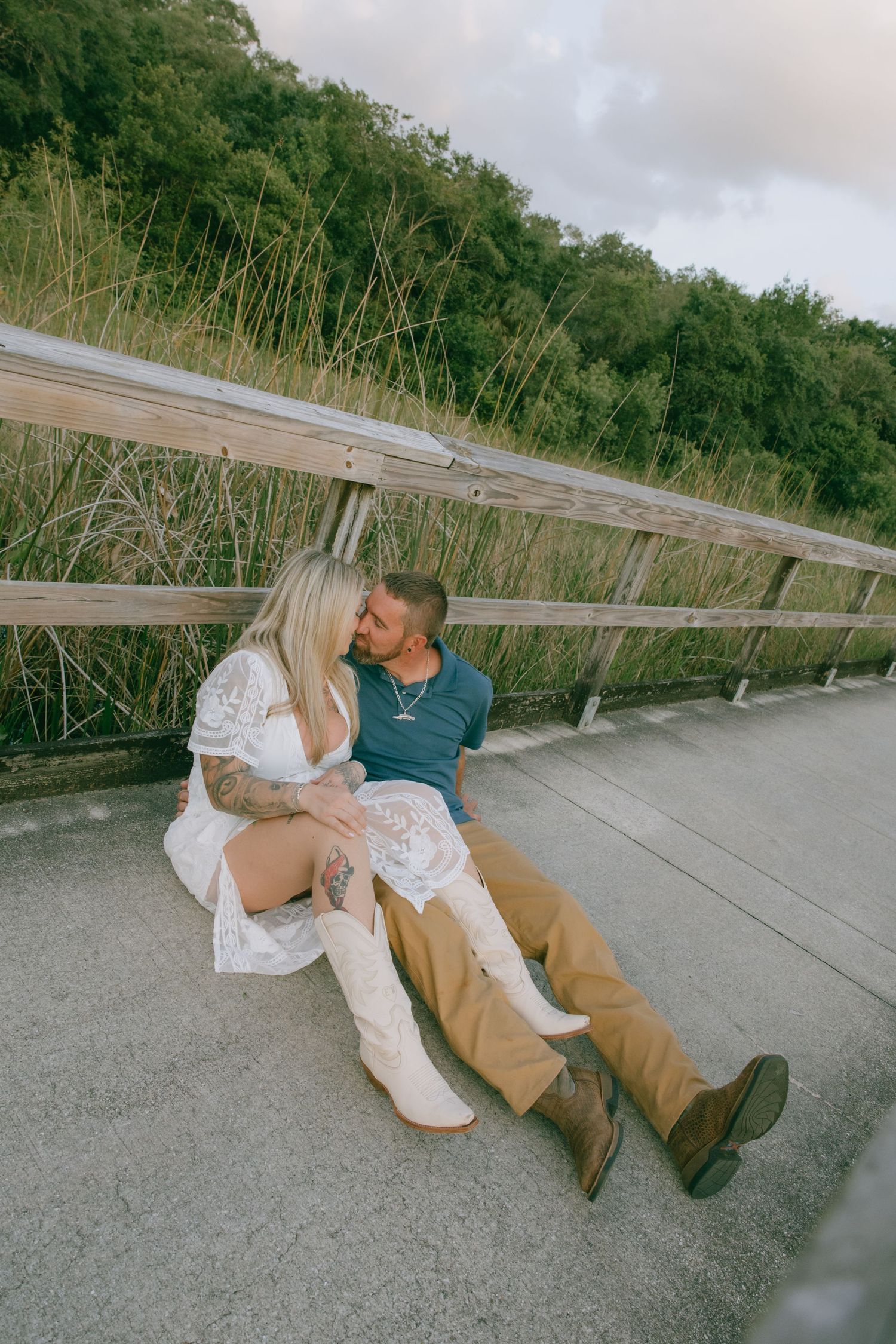 A couple sits close together on a wooden boardwalk surrounded by natural marsh scenery.