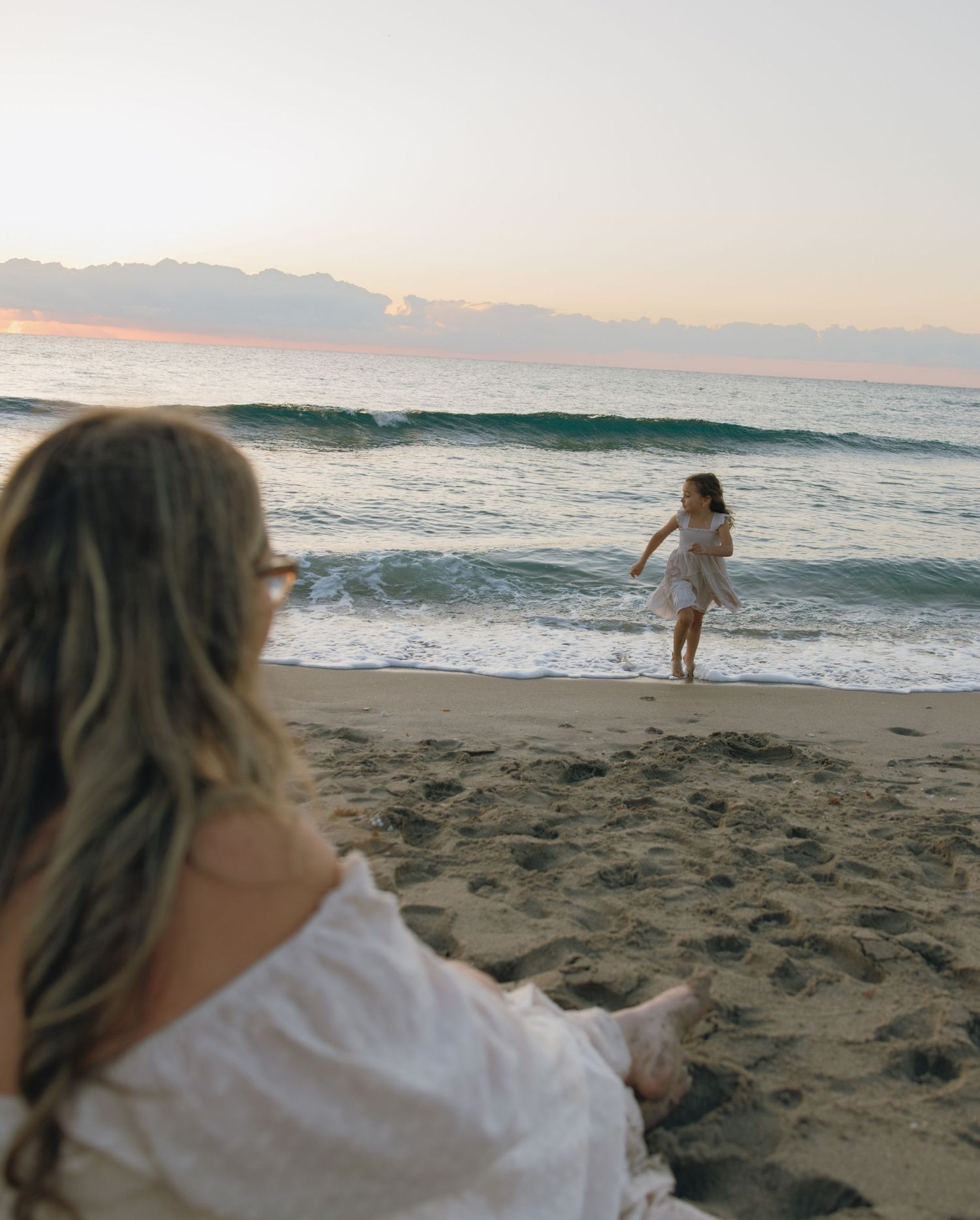 A person in white clothing relaxes on the beach as waves roll in during golden hour.