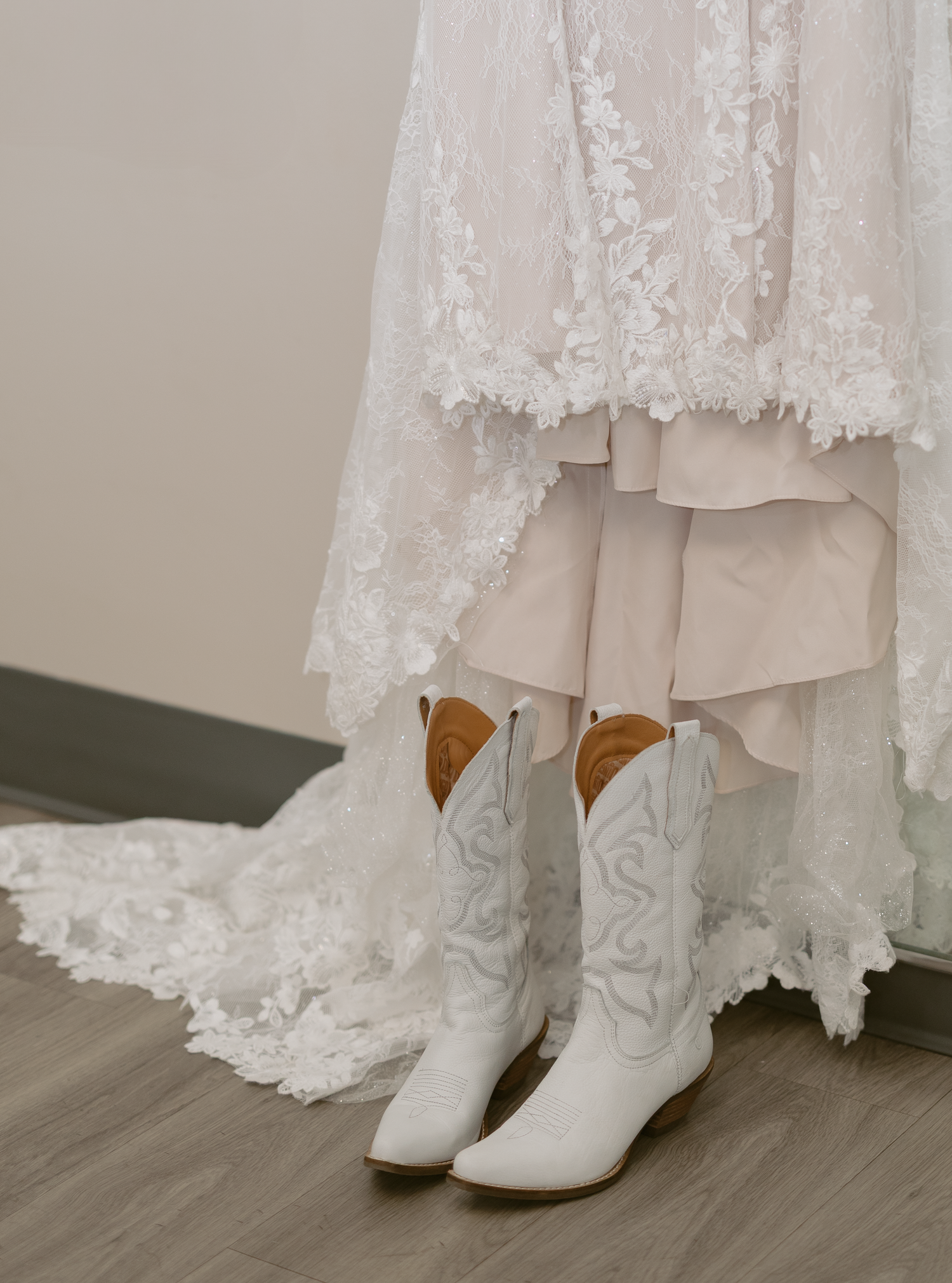 White cowboy boots with floral embroidery peek out from under an elegant lace wedding dress.