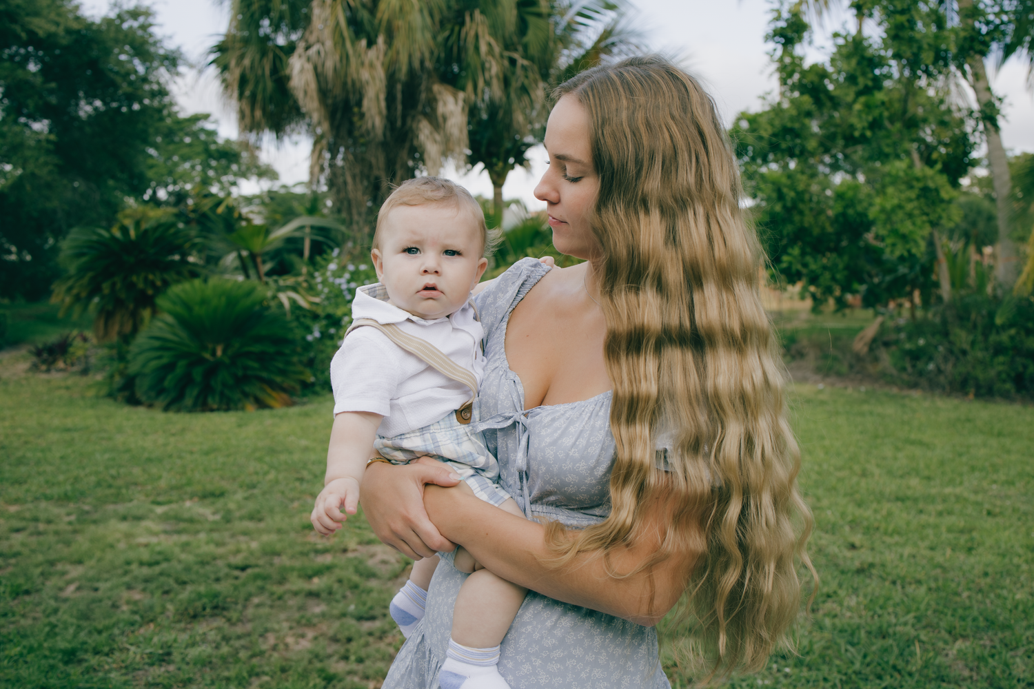 A tender outdoor portrait of a mother holding an infant in summery attire.