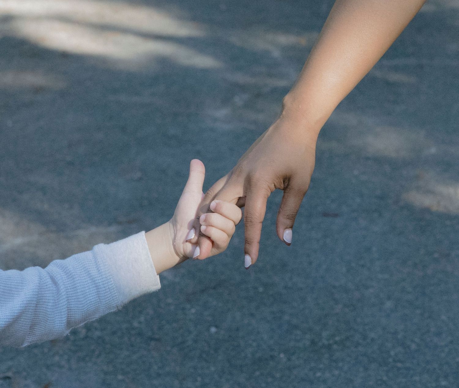A hand reaches down to draw with chalk on a dark asphalt surface in a sequence of four connected images.