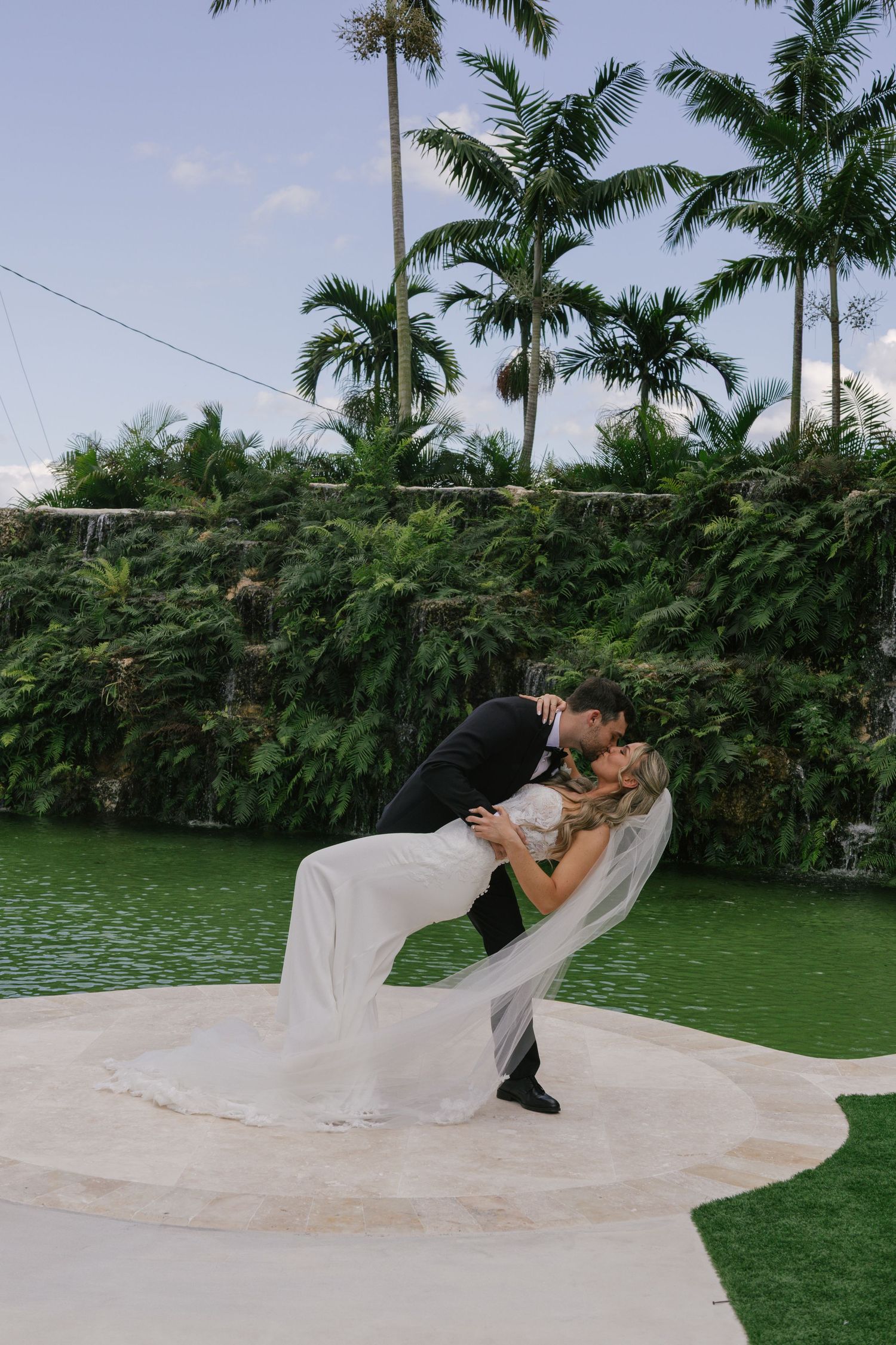 A romantic wedding photo sequence showing a dramatic dip pose on a green lawn with palm trees in the background.