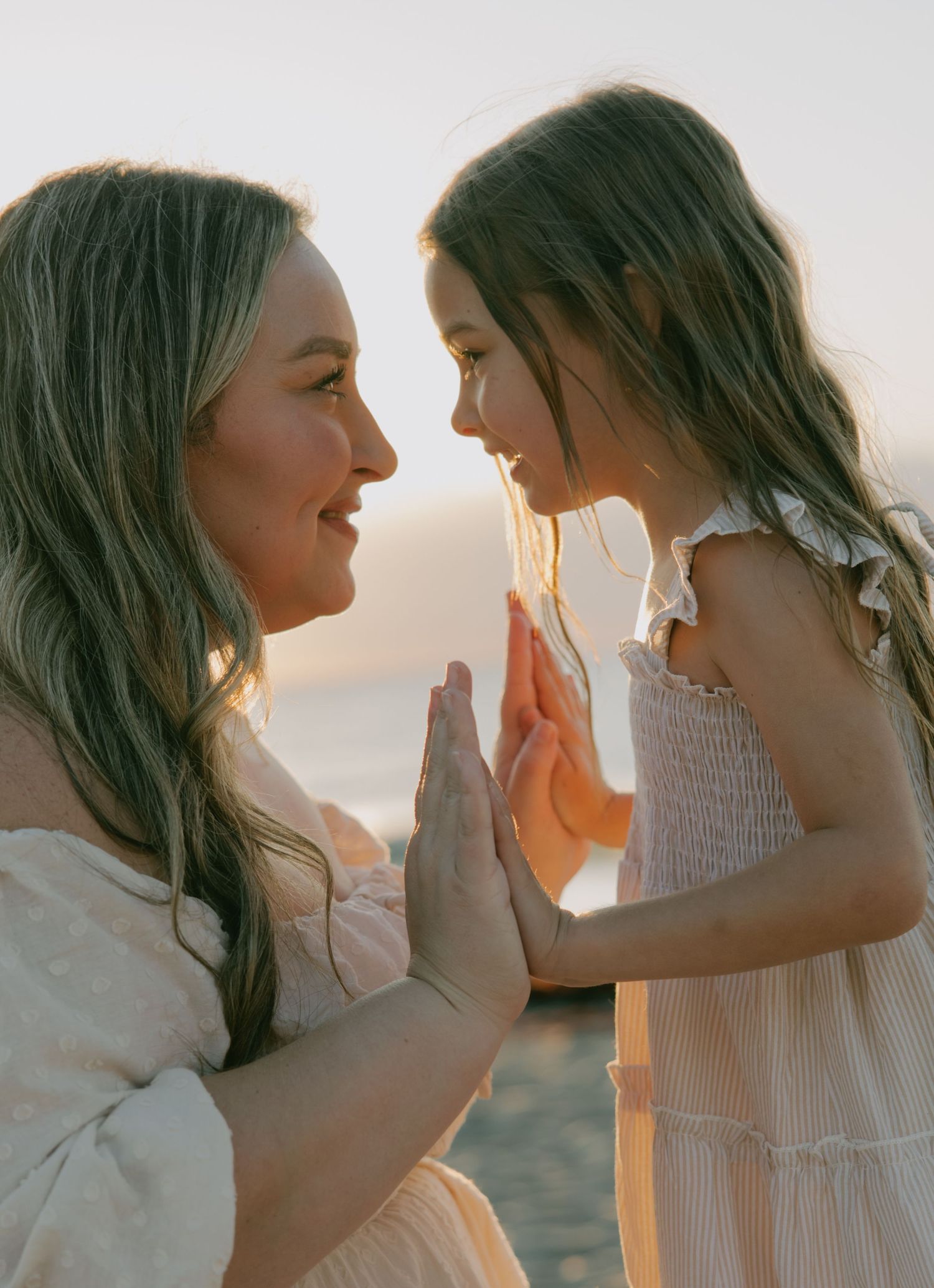 Two people in white outfits share a playful moment on the beach at sunset.