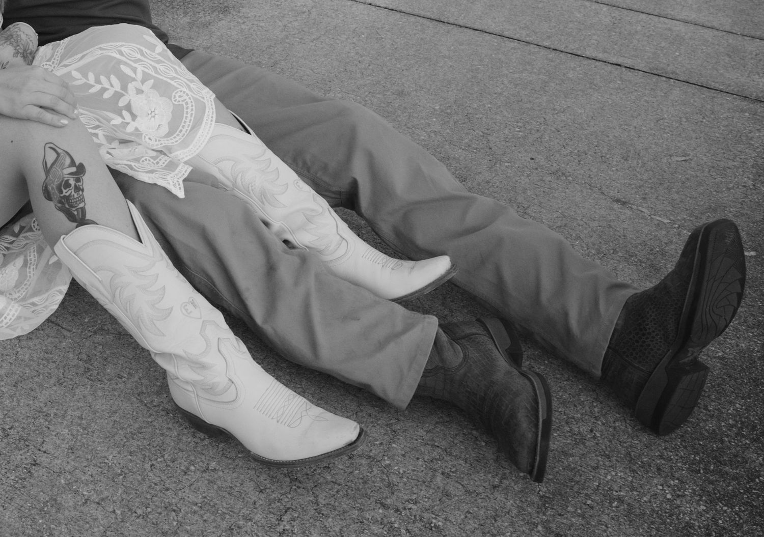 Black and white photo of contrasting cowboy boots and work boots on pavement.