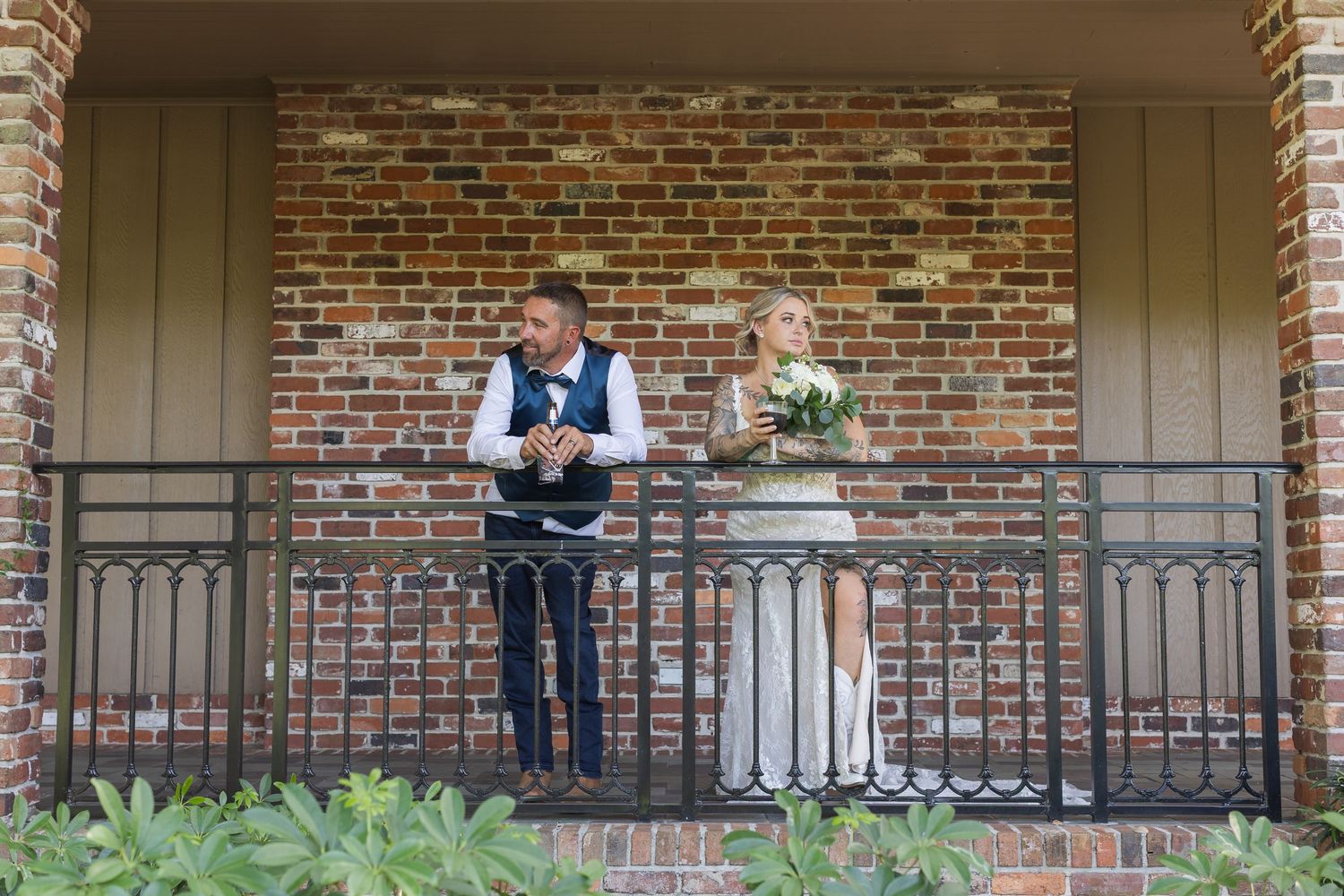 Couple standing on a brick porch with iron railings during their wedding day.