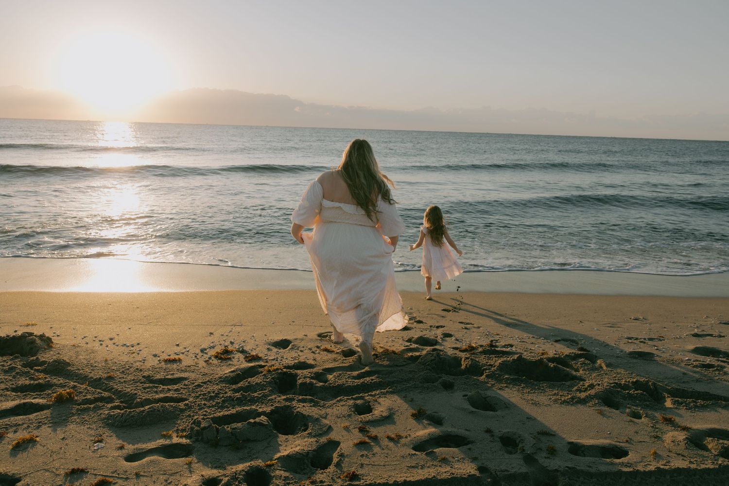 Panoramic beach scene at sunset with people in white clothes walking along shoreline.