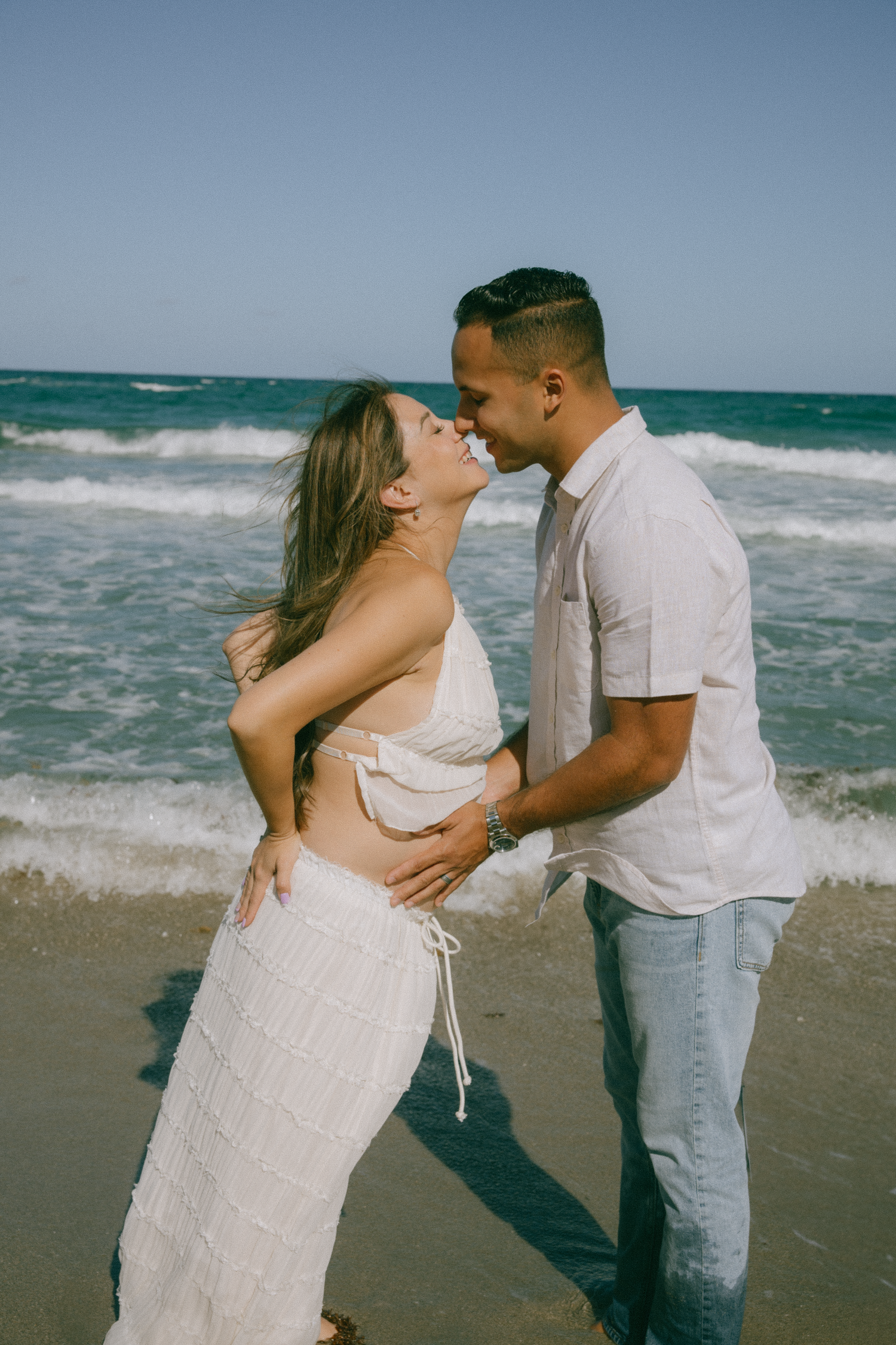 A couple shares romantic moments on a beach with crashing waves in the background.