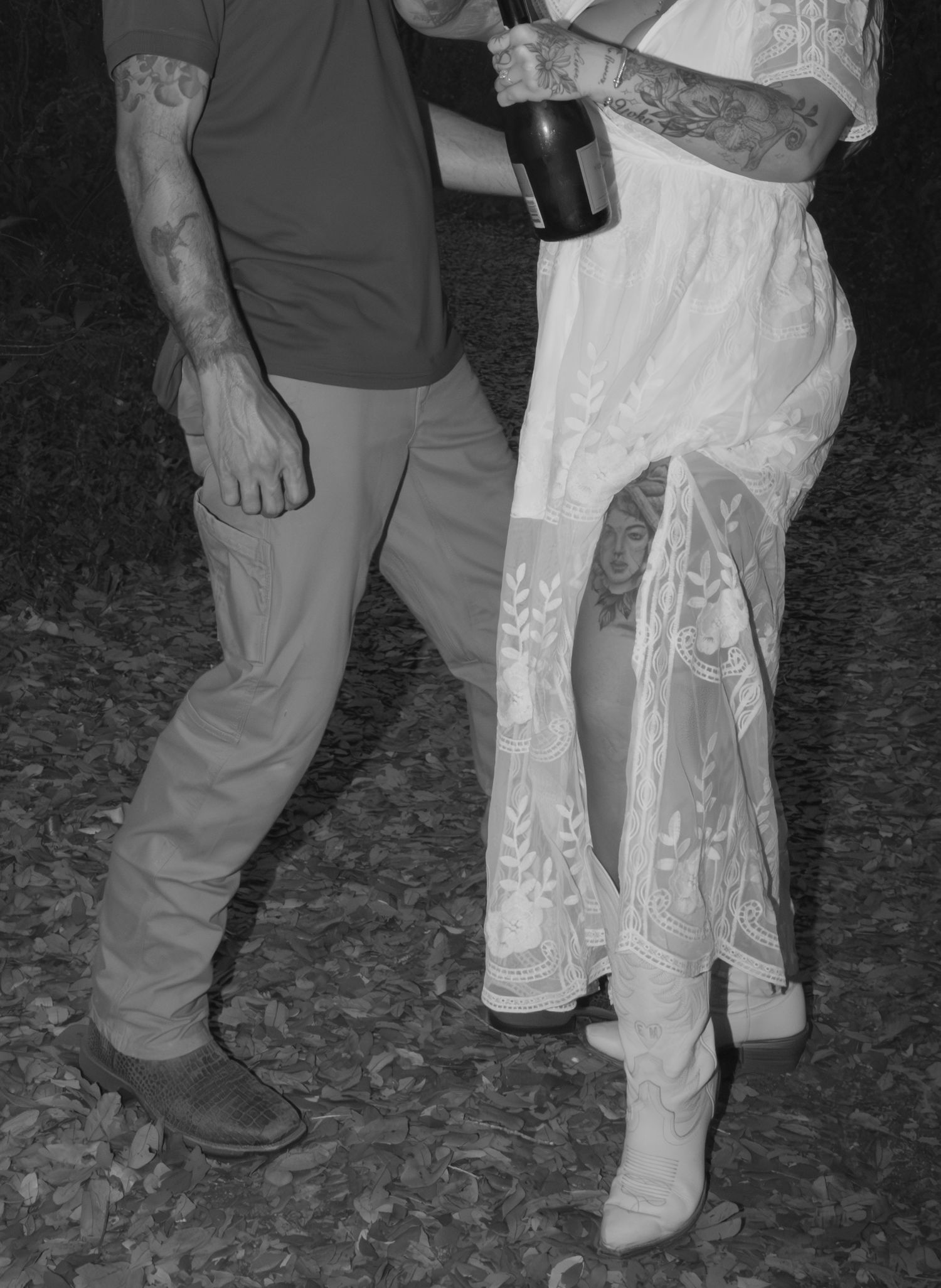 Close-up of two people's legs, one in white lace dress and cowboy boots, another in casual wear.