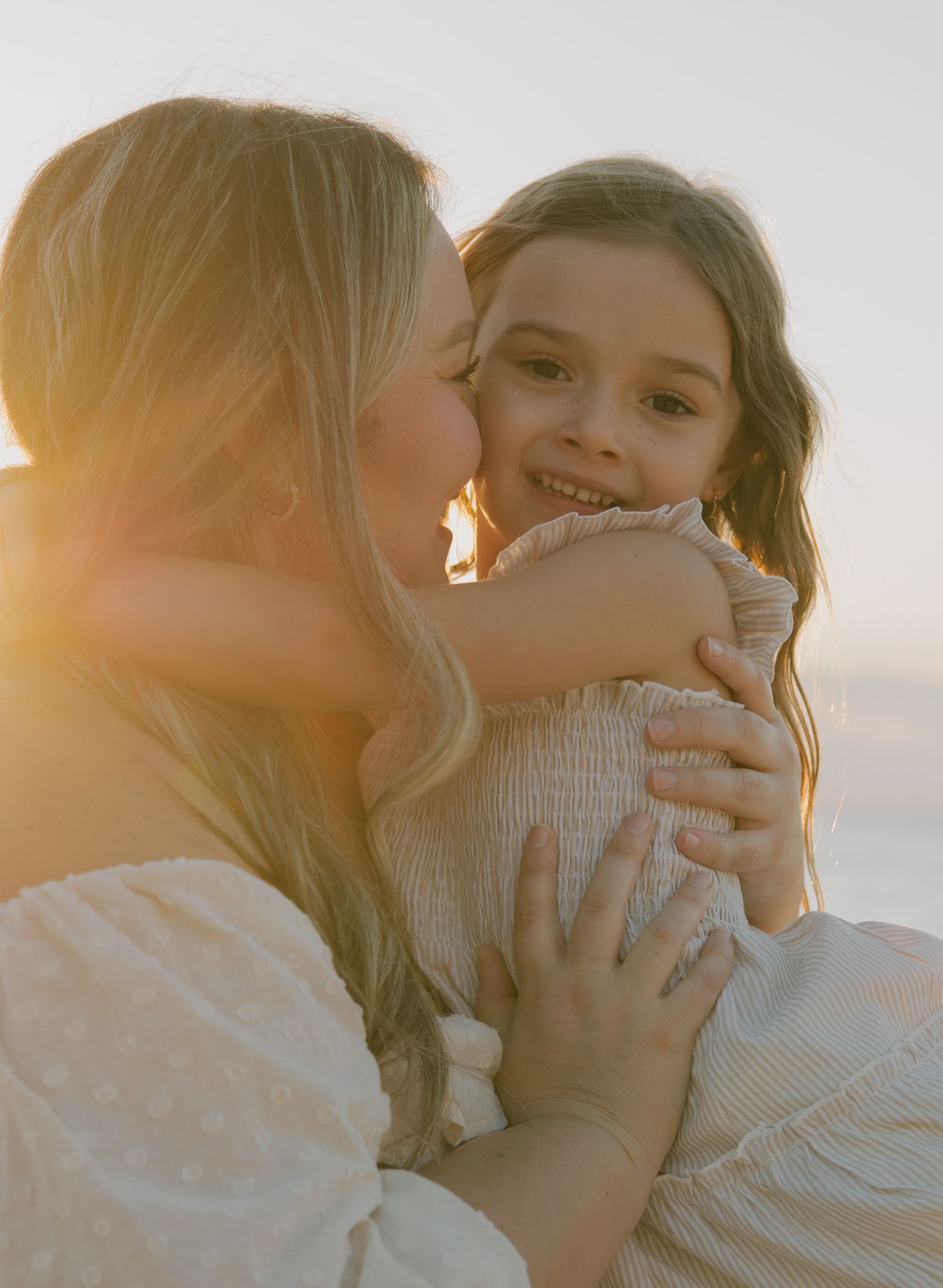 Two people share a warm embrace on the beach during golden hour.