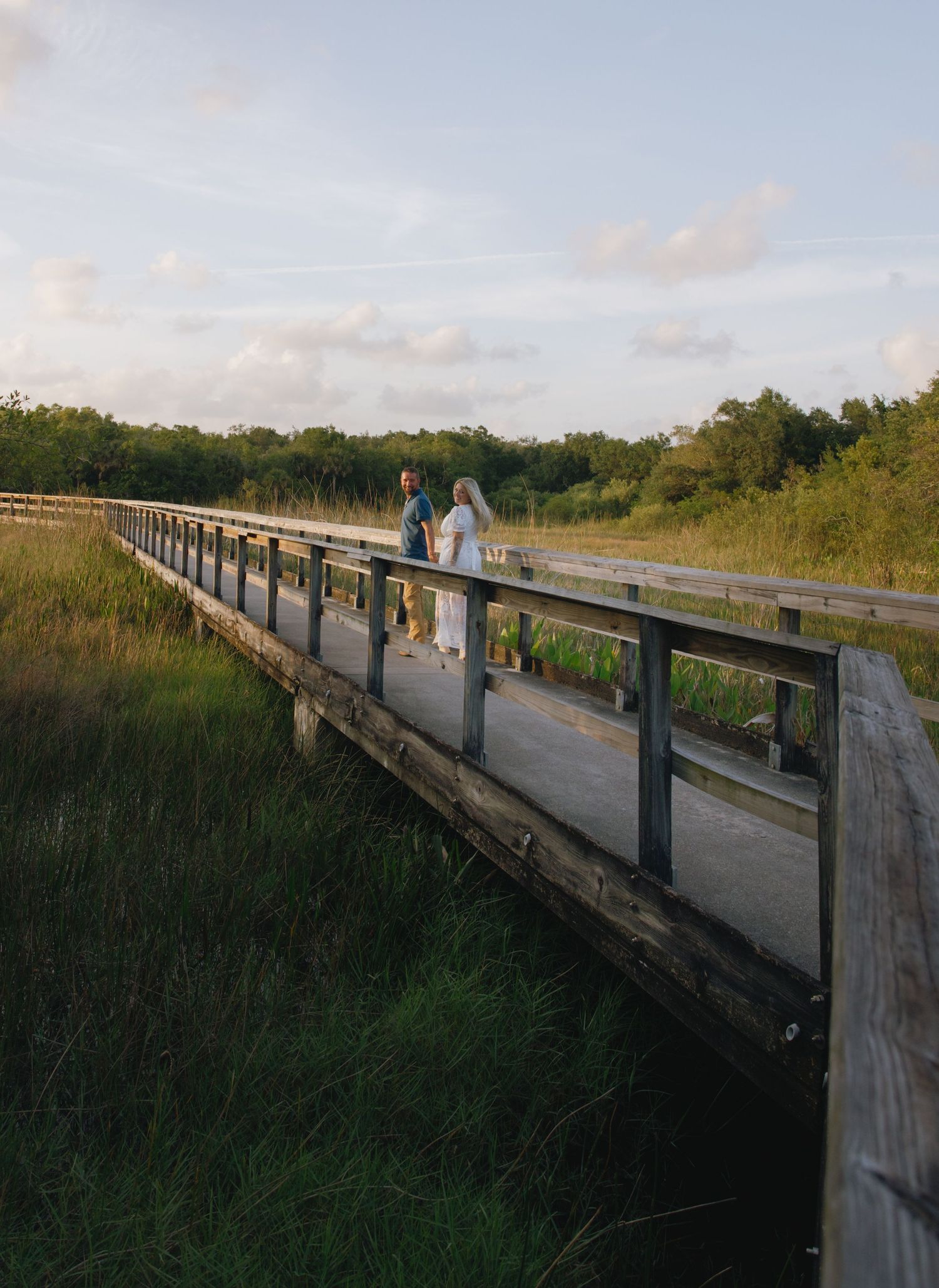 Wooden boardwalk stretching across a scenic marsh area during sunset.