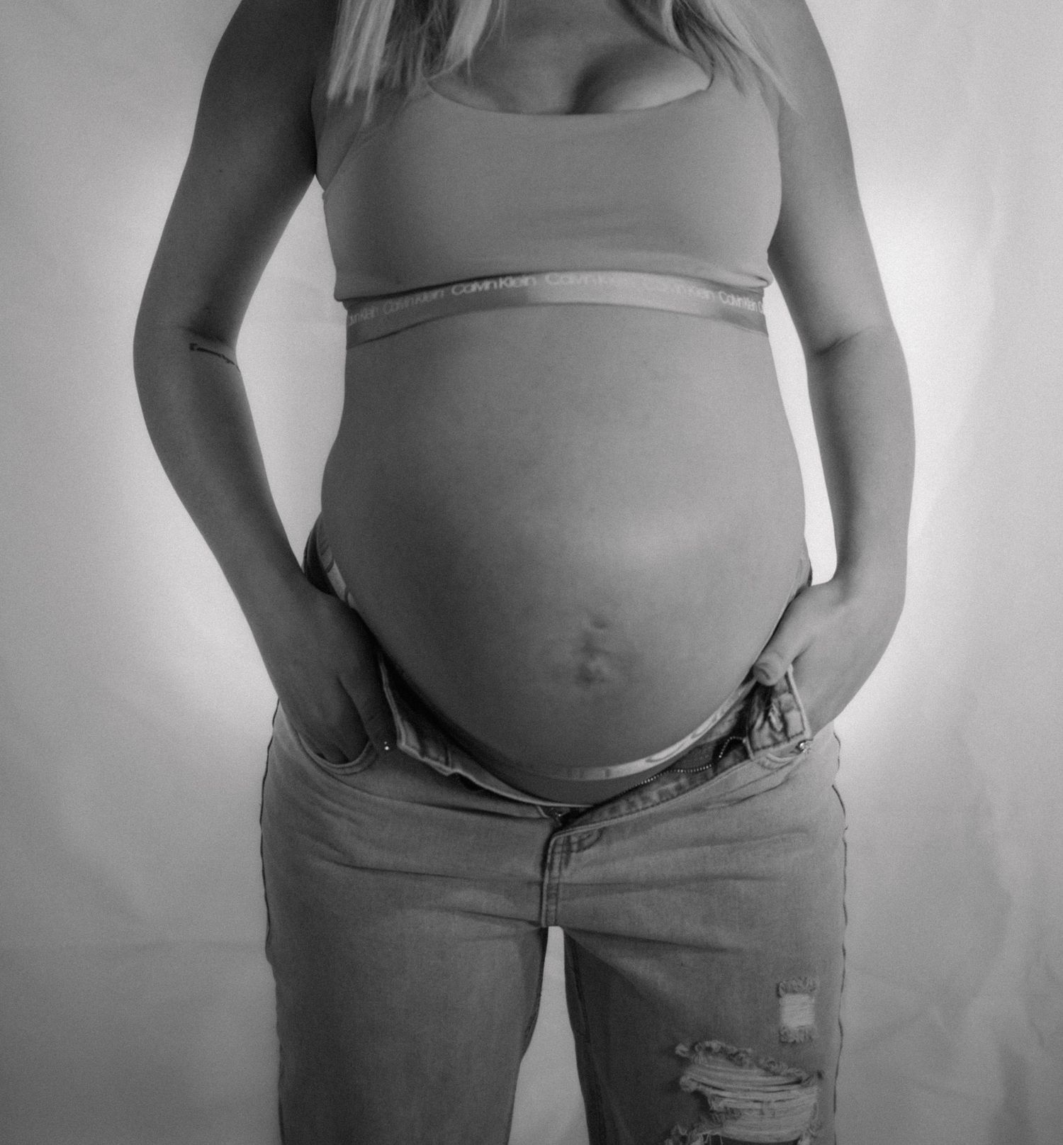 Black and white photo of pregnant belly in distressed denim jeans.