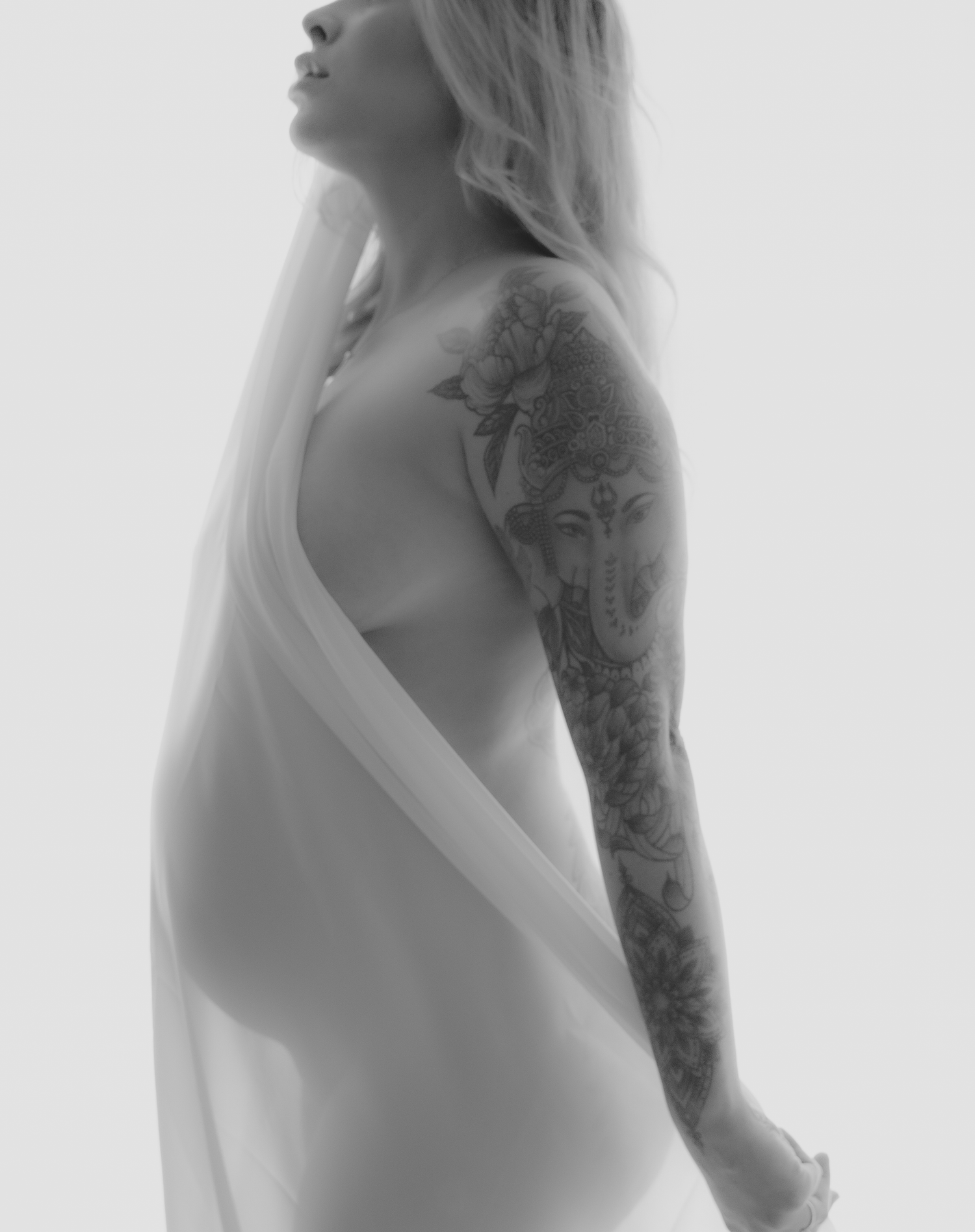 Artistic black and white maternity photo showing tattoo sleeve and draped fabric.