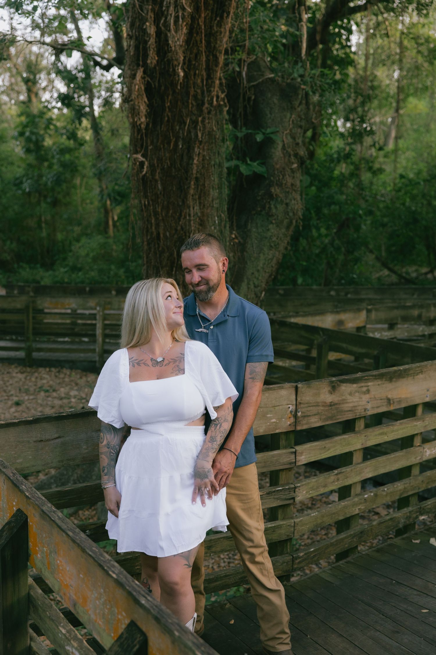 A couple shares a romantic moment on a wooden deck surrounded by lush trees in an outdoor setting.