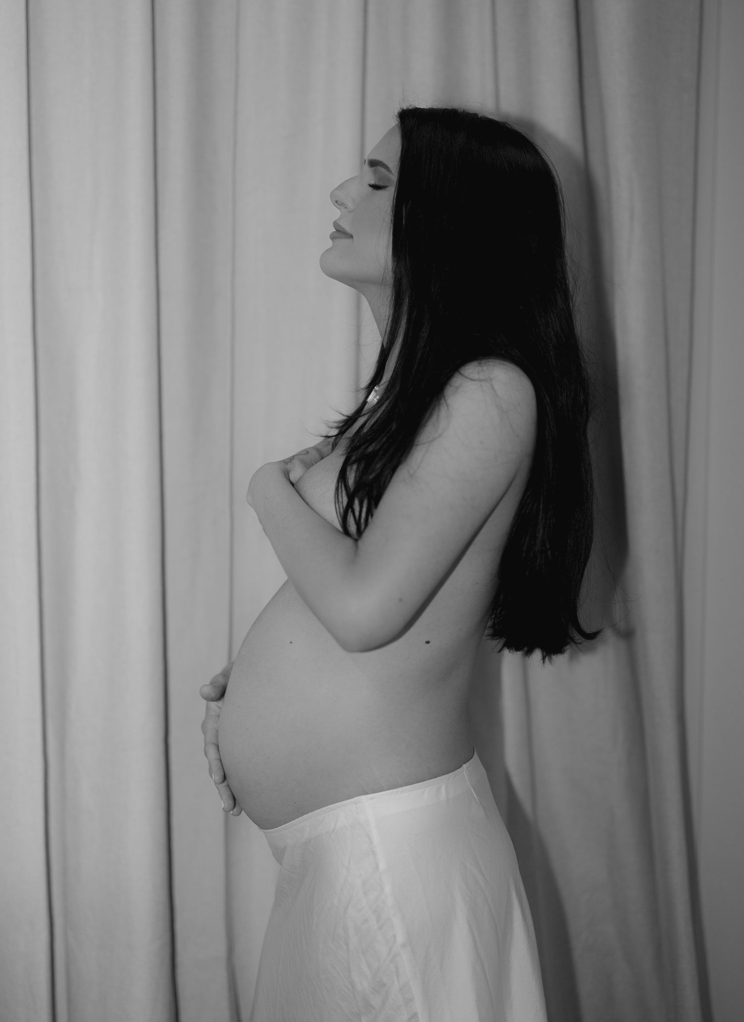 Black and white artistic pregnancy photoshoot series showing poses against a curtained backdrop.