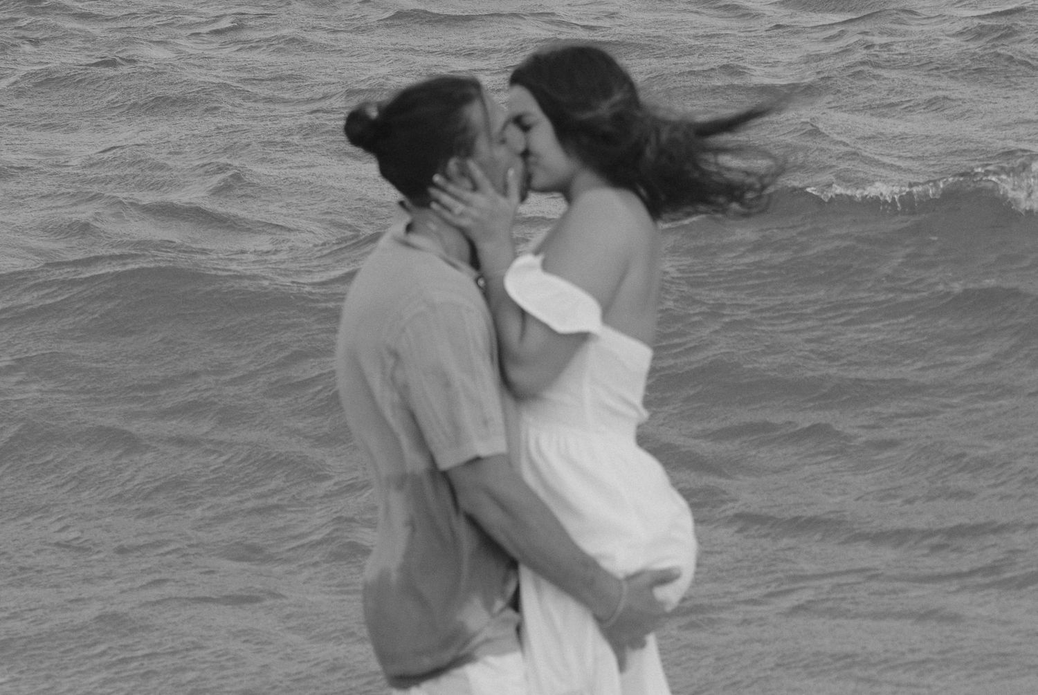 A romantic black and white photograph shows a couple embracing and kissing in the ocean waters.