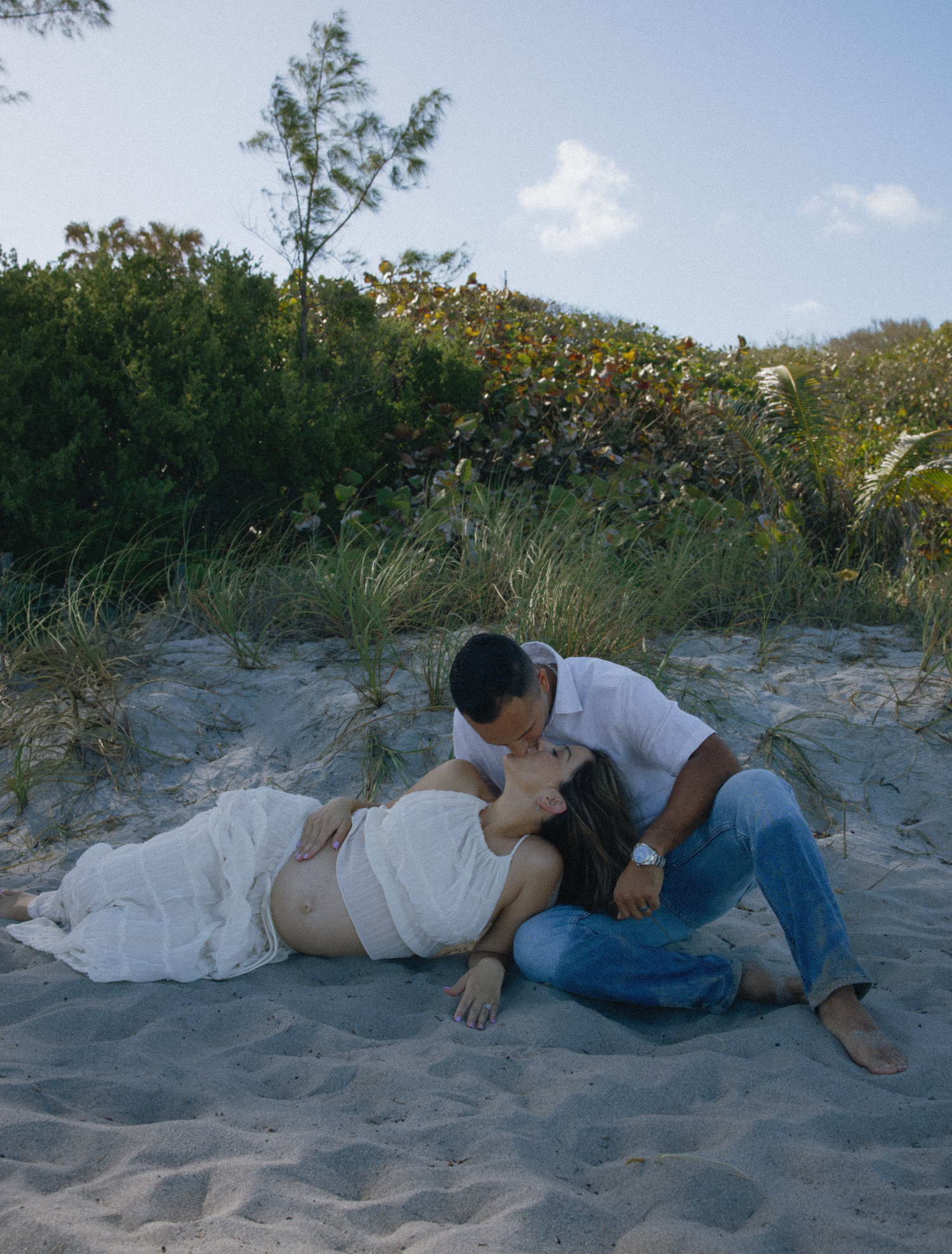 Romantic couple sharing an intimate moment on a sandy beach against a backdrop of lush vegetation.