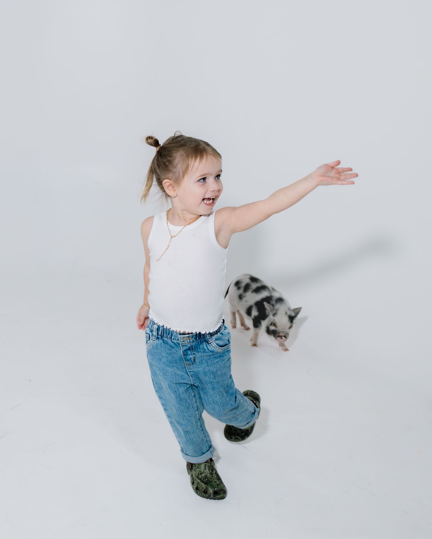 A small child wearing jeans and a white shirt performs a dynamic dance move against a light gray background.