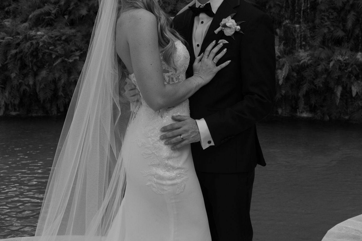 A couple in wedding attire shares an intimate moment by a lake during their outdoor ceremony.