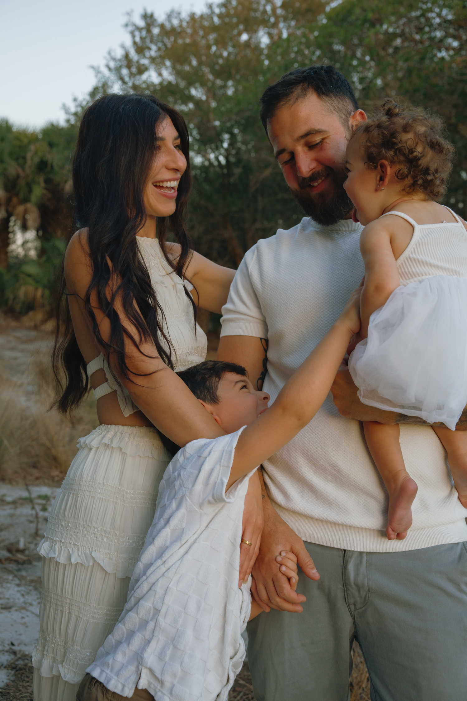 Family shares intimate moment outdoors in white and neutral outfits during golden hour photoshoot.