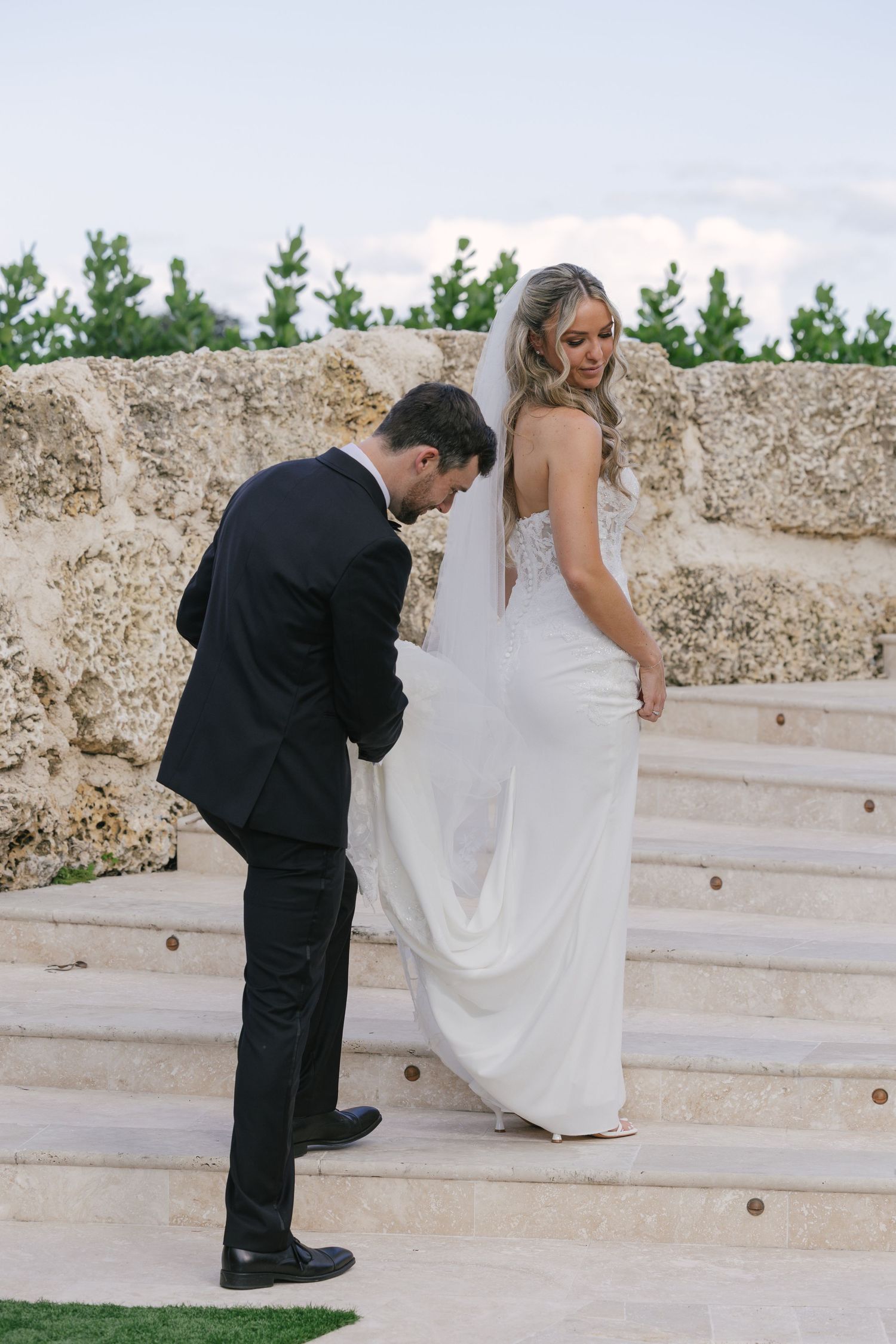 A couple on stone steps during their wedding day, with the bride in white dress and groom in black suit.