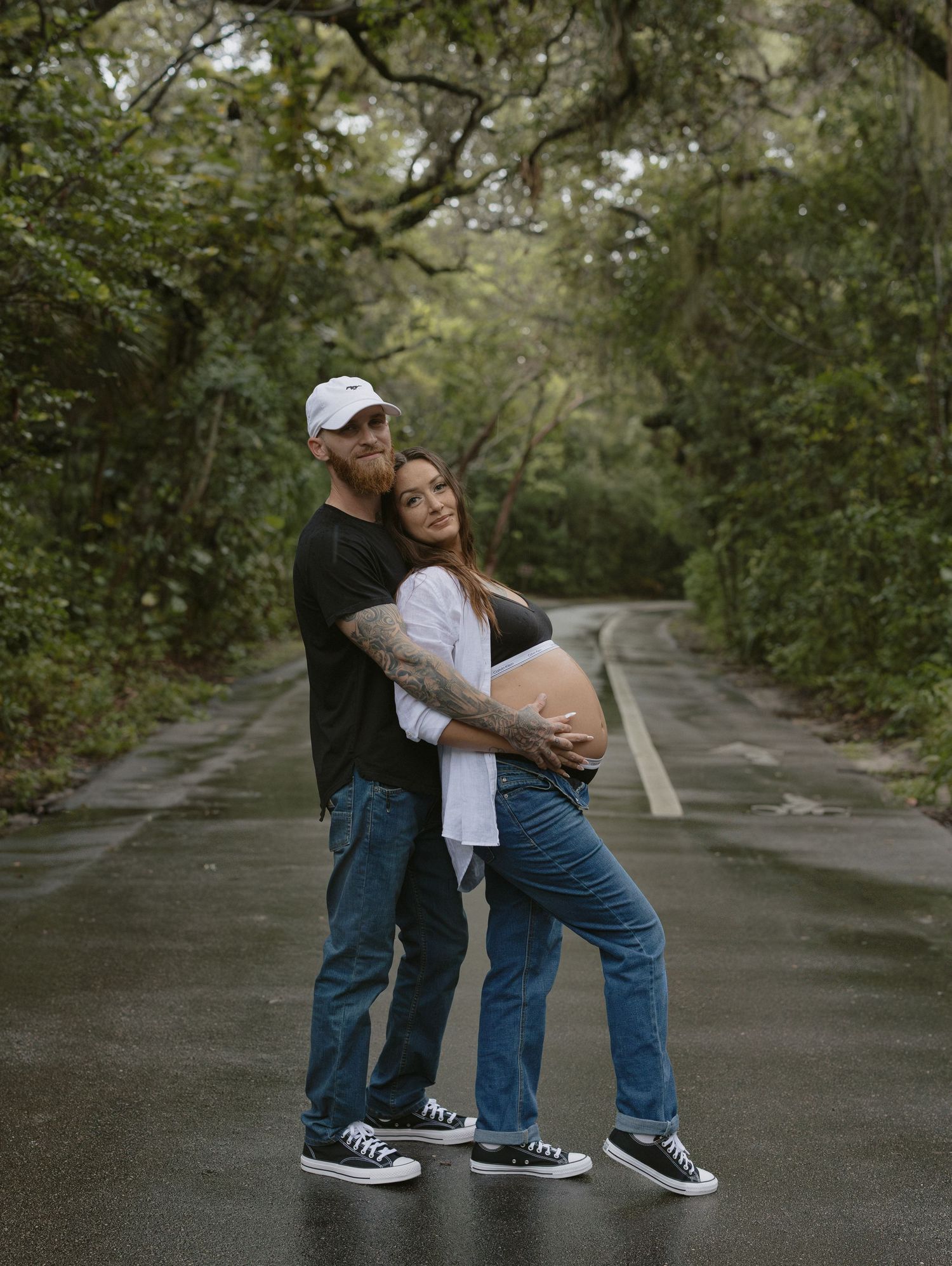 Couple sharing romantic moments on a tree-lined path during an outdoor photoshoot session.