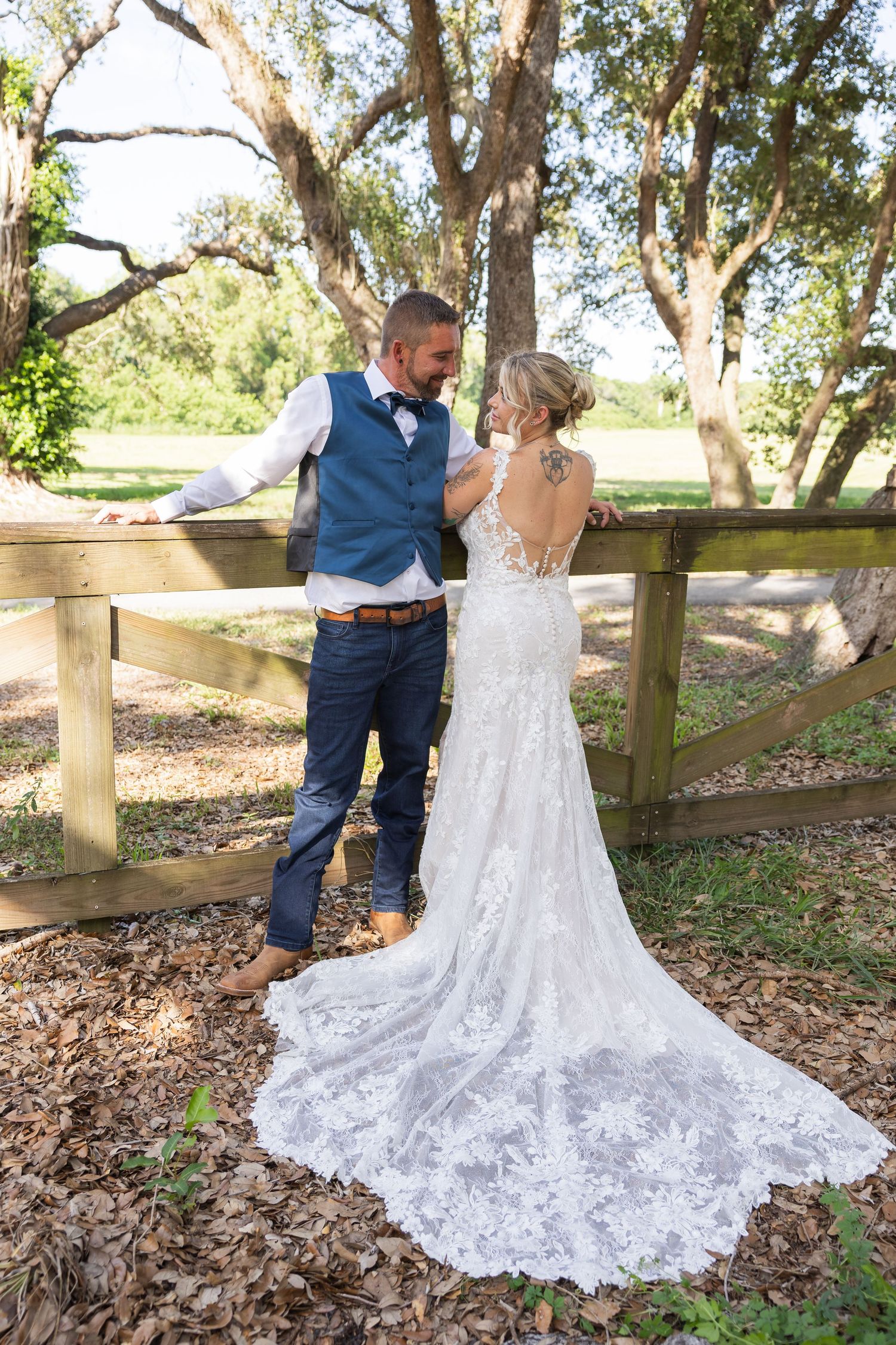 A couple in wedding attire poses romantically against a rustic wooden fence in an outdoor garden setting.