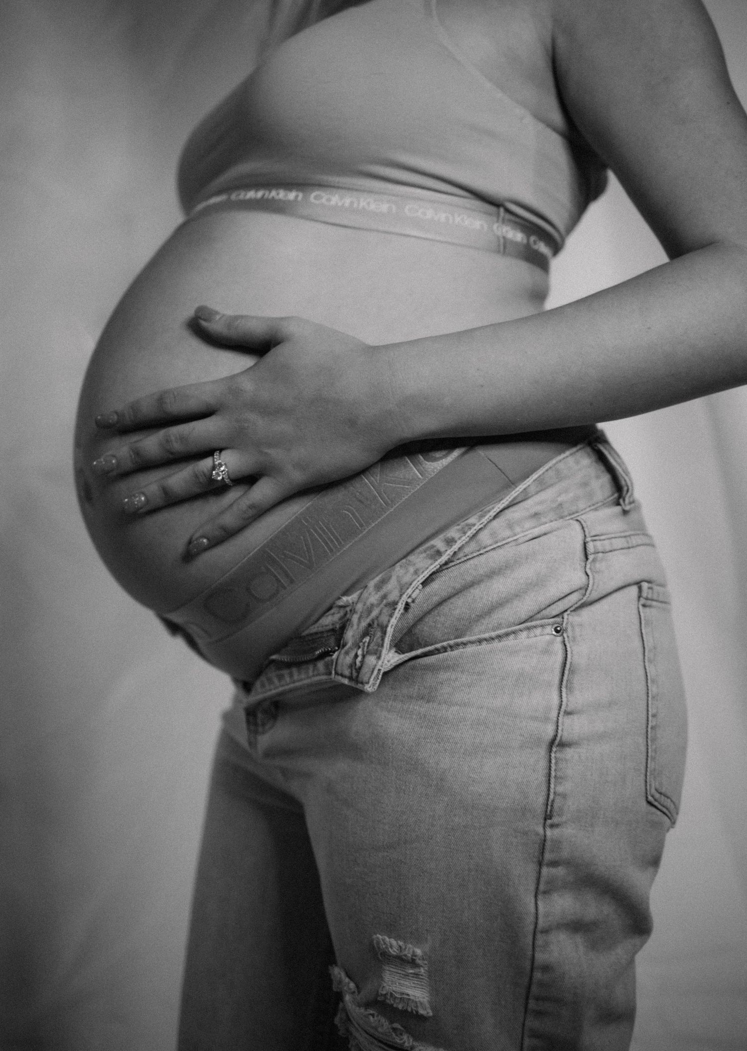 A black and white side view photo highlighting a pregnant belly with a gentle hand placement.