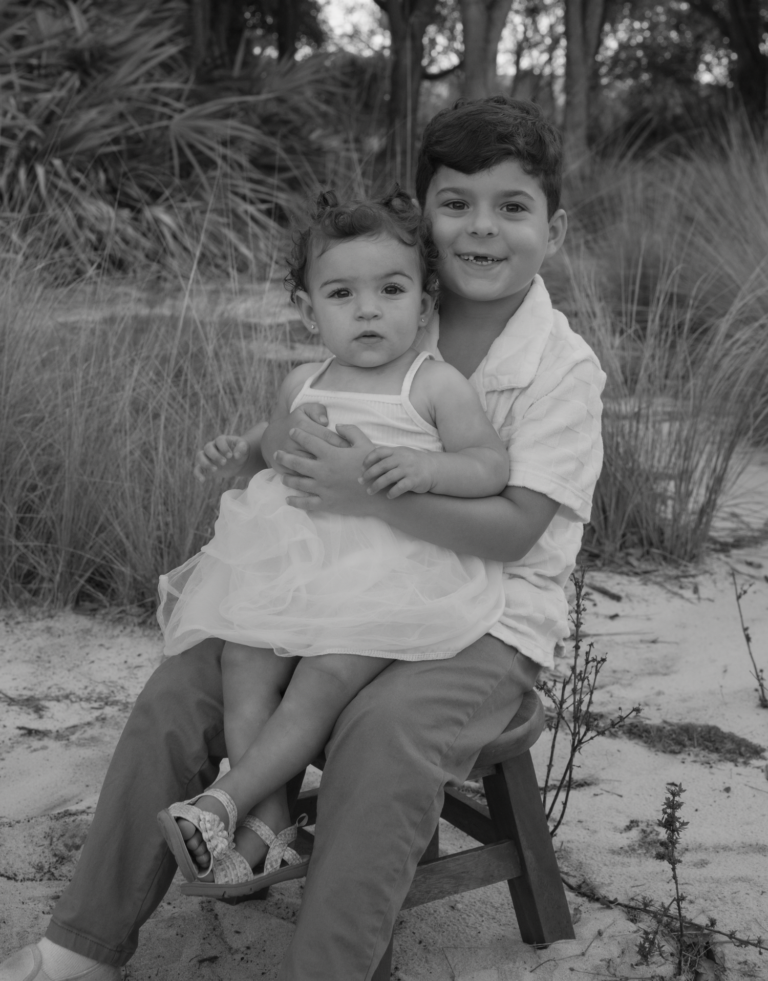 Black and white portrait of siblings sharing a tender moment outdoors.