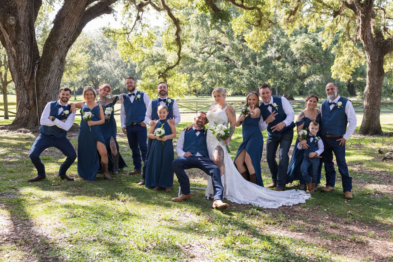 Wedding party and guests gathered under large oak trees in an outdoor setting.