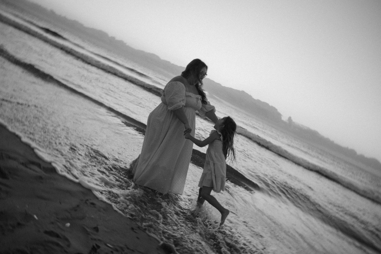 A black and white photo captures two people walking hand in hand along the beach.