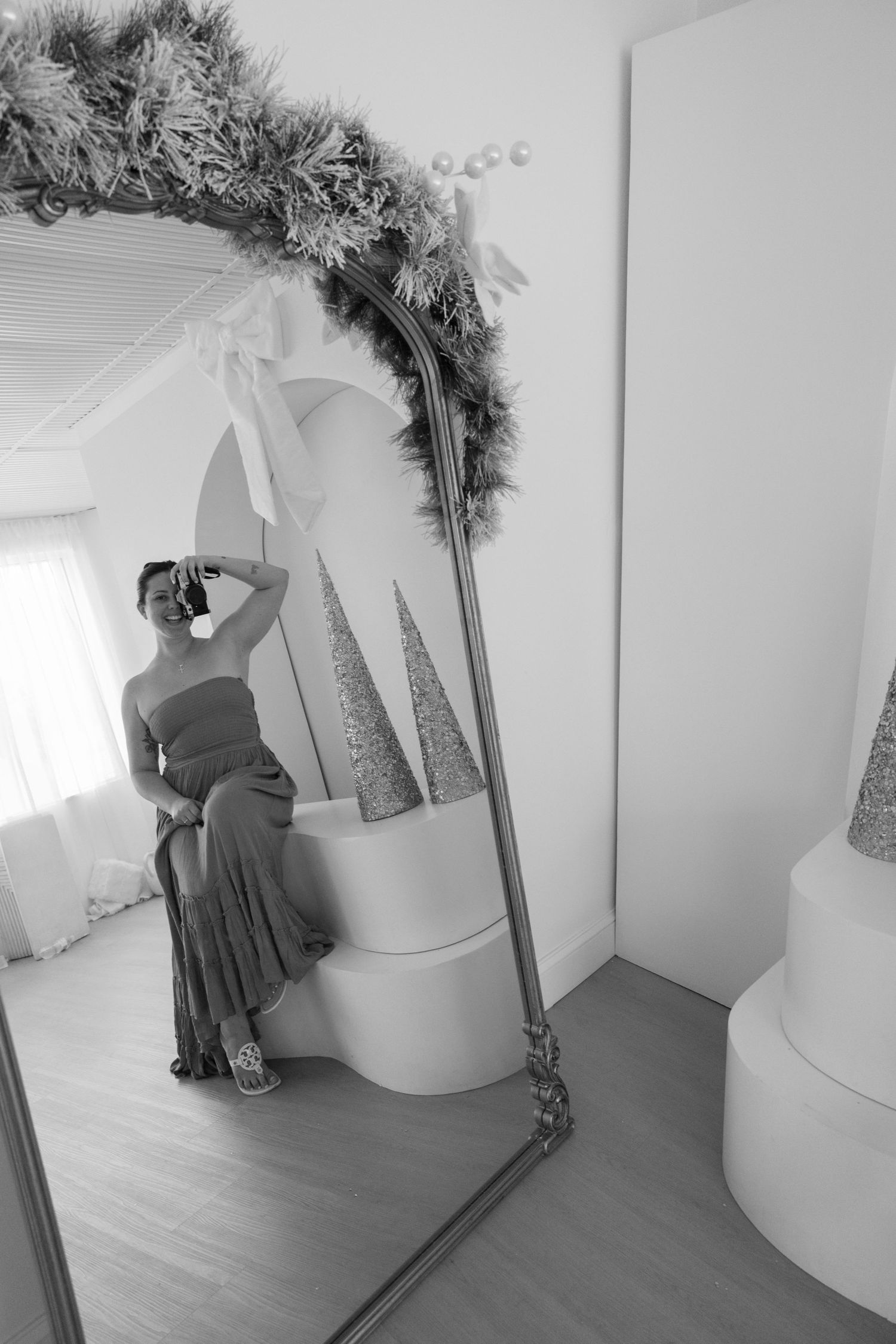 Black and white image series showing someone decorating a cylindrical pedestal with evergreen garland in an interior space.