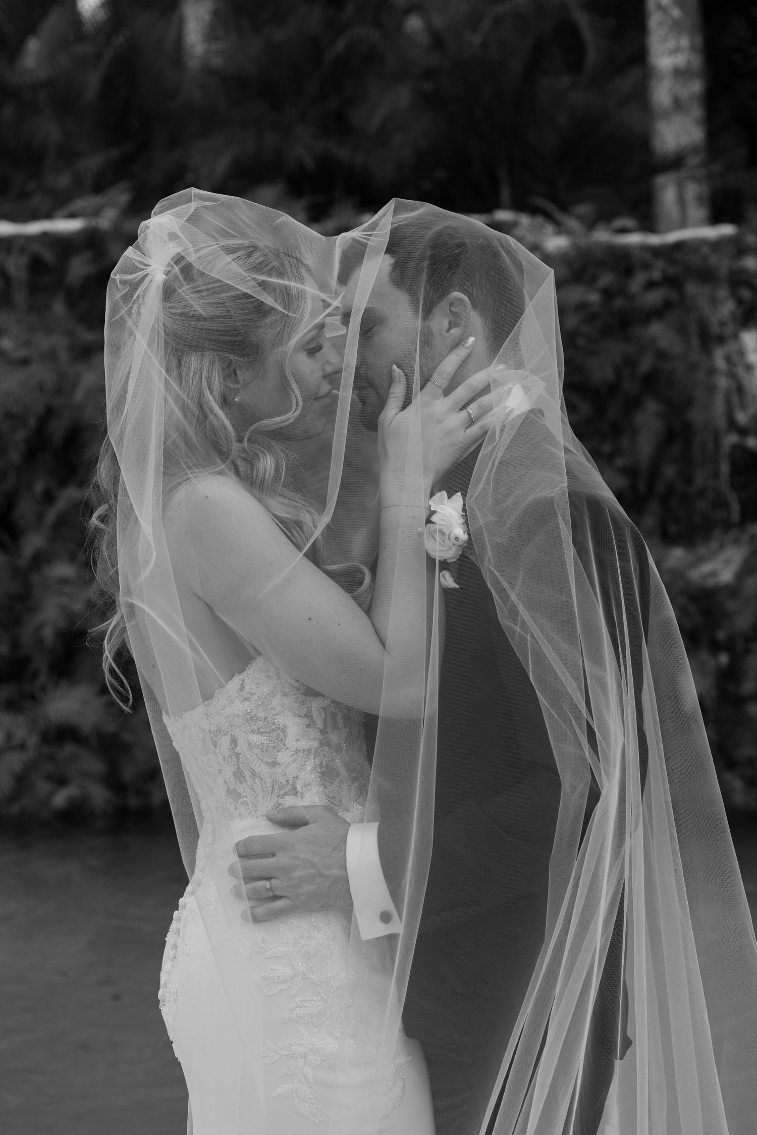 A romantic black and white wedding photo series showing a couple kissing under a flowing white veil.