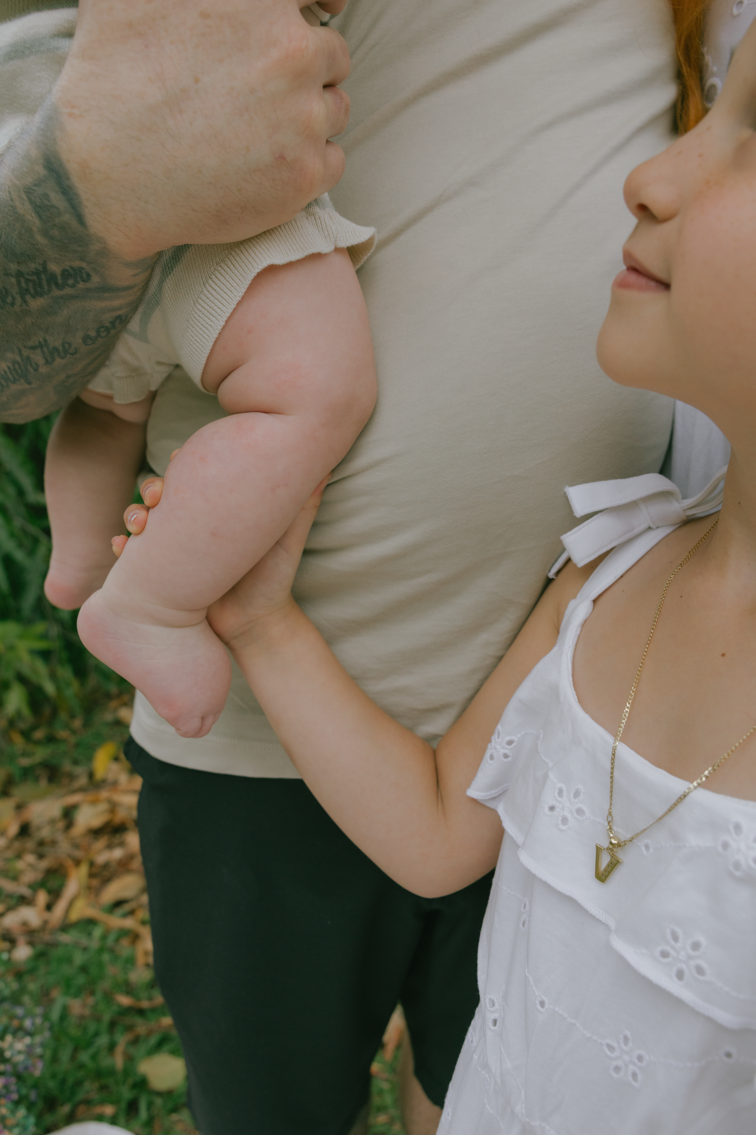 Close-up shots of a parent in black clothing holding a baby wearing a white eyelet dress against a natural outdoor backdrop.
