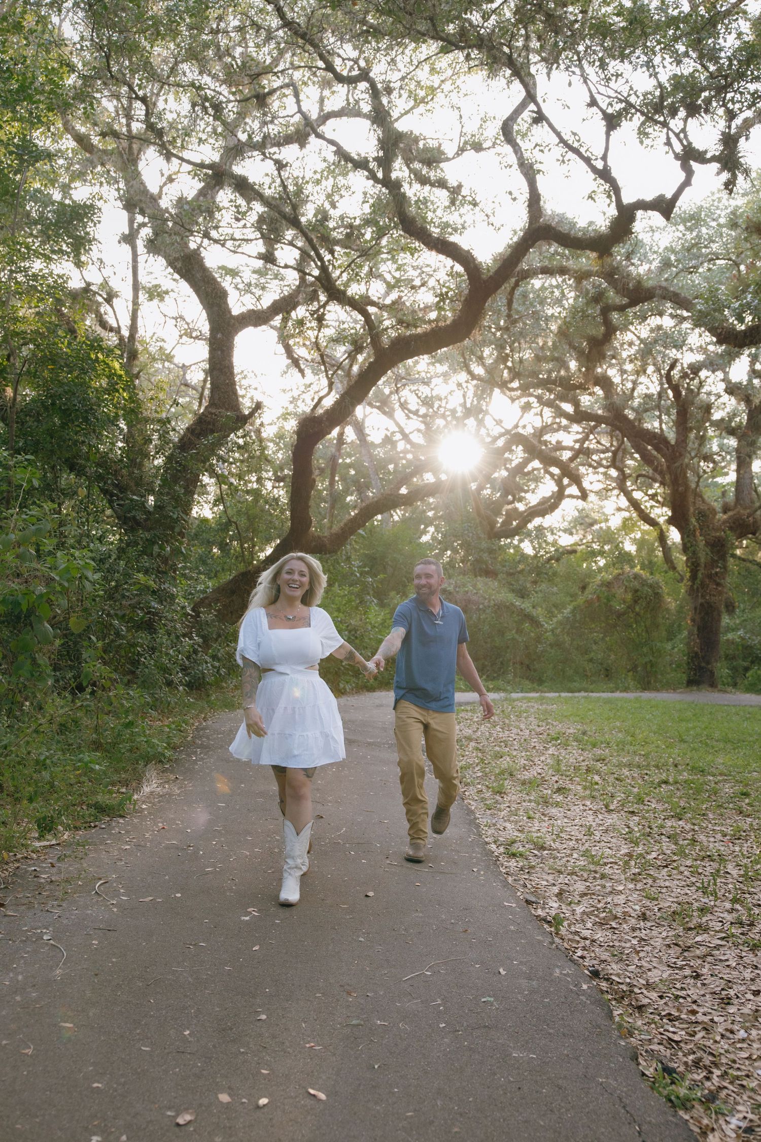 Couple strolling along a pathway surrounded by sunlit oak trees.