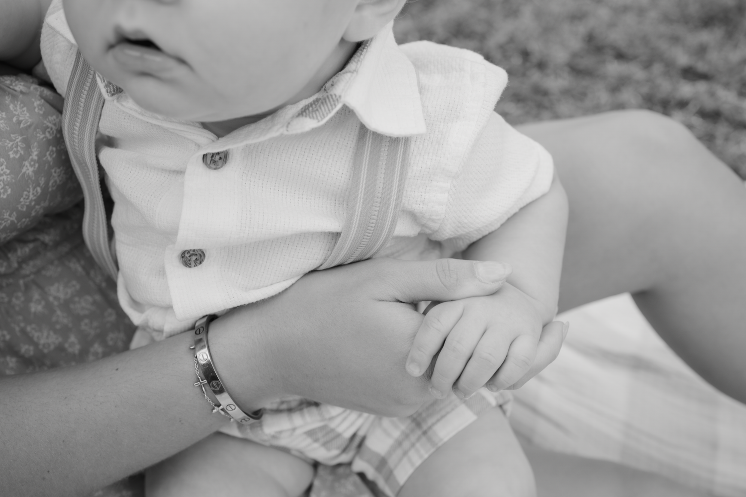 Close-up details of baby's hands and white clothing during outdoor photoshoot.