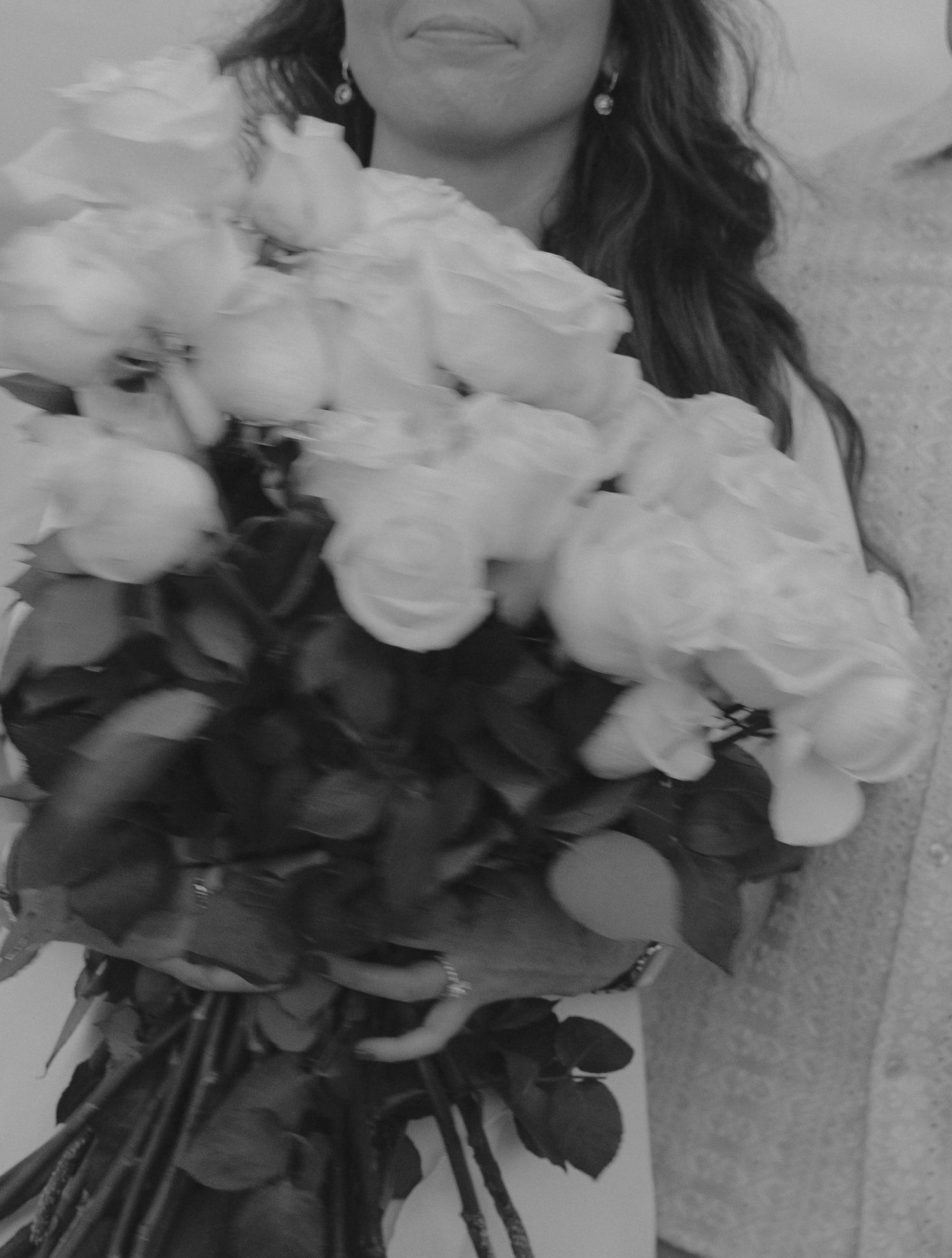 A close-up black and white photo of a bridal bouquet with white roses and flowing ribbons.