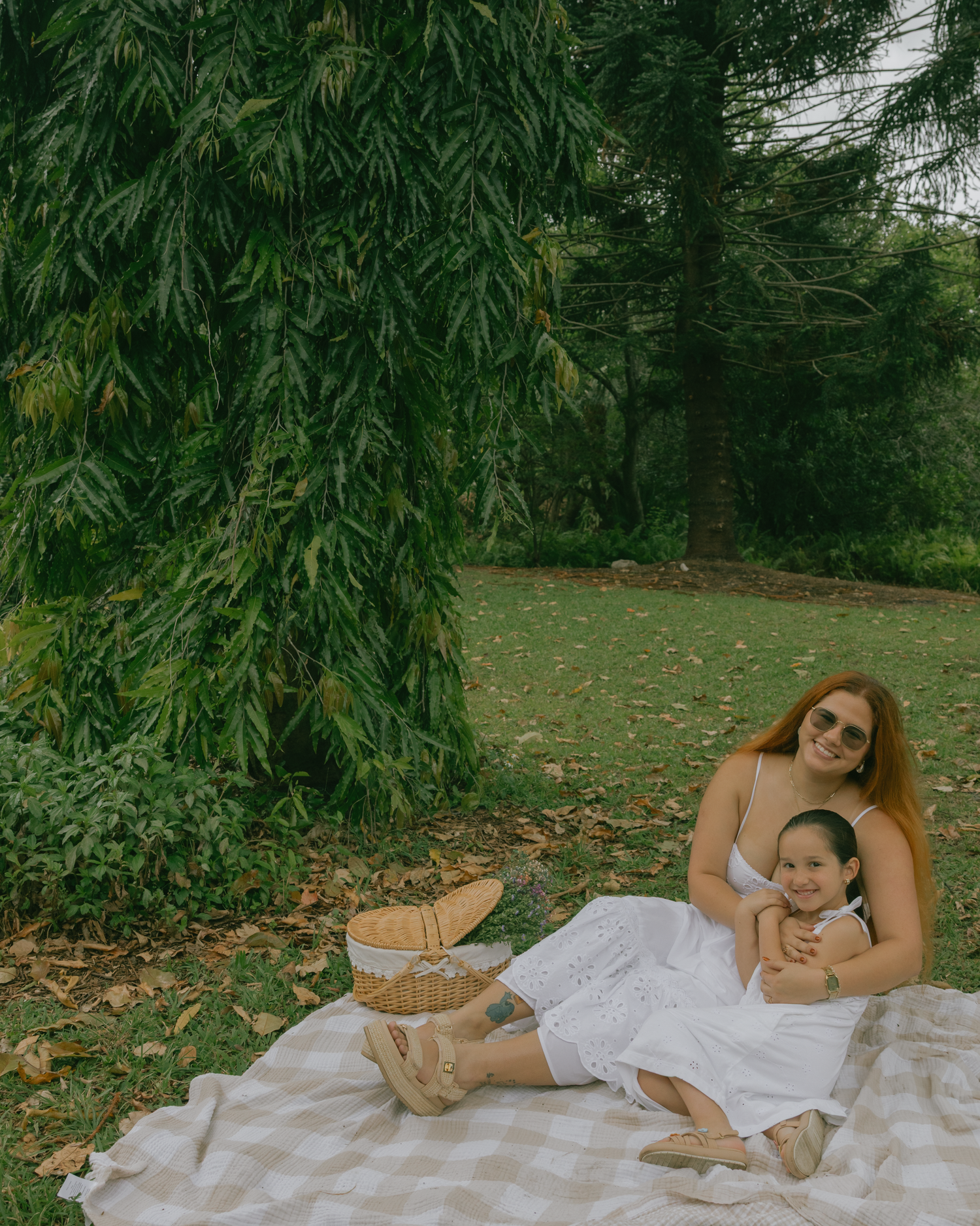Mother and child relaxing on blanket during outdoor picnic with wicker basket nearby.