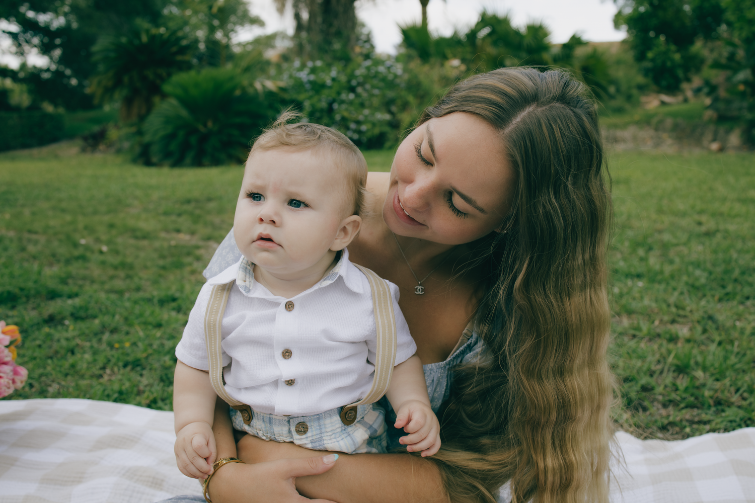 Intimate outdoor portrait session with infant in white and grey outfit against natural backdrop.
