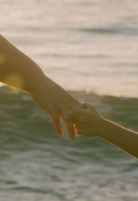 Hands reaching toward ocean waves during golden hour sunset.
