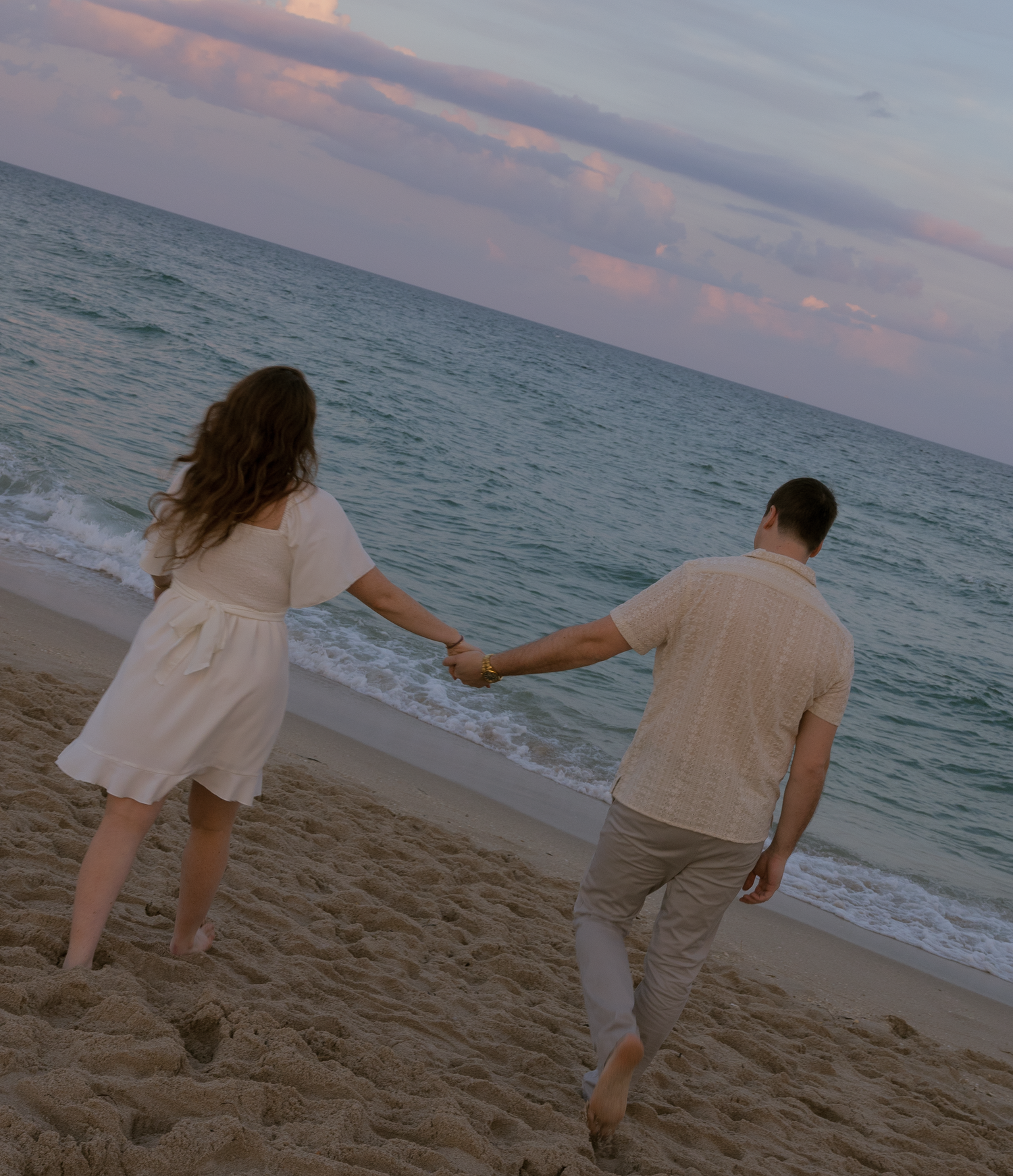 A couple walking and playing together on a beach during sunset with ocean waves in the background.