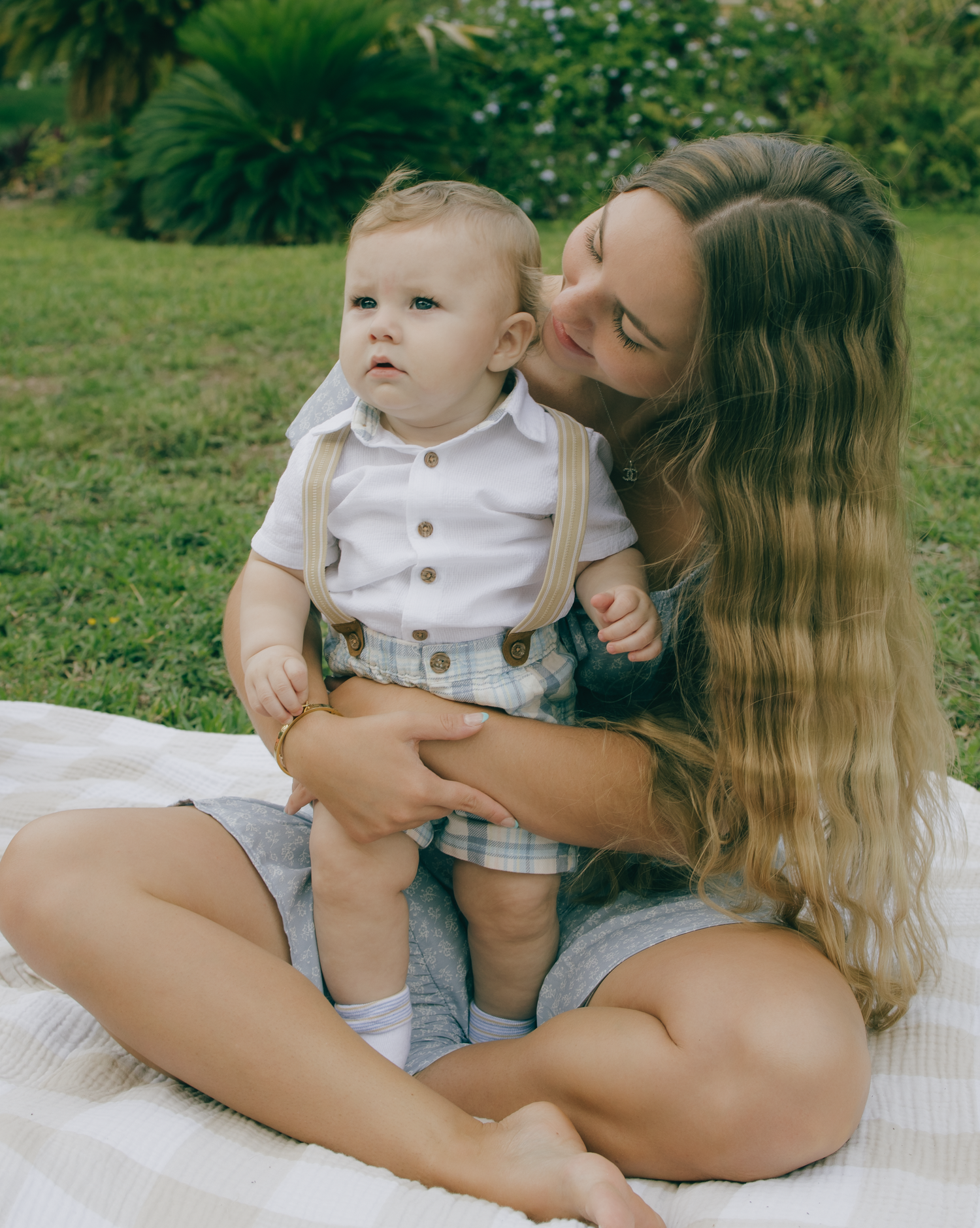 Sweet bonding moment on a picnic blanket surrounded by greenery and palm trees.
