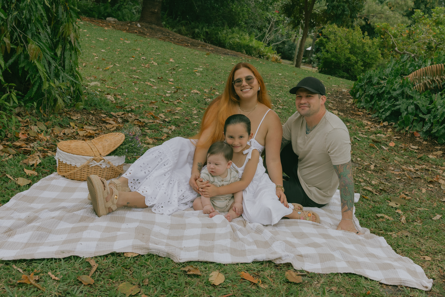 Family relaxing on picnic blanket during outdoor photo session.